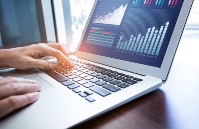 a man types on a laptop keyboard while looking at analytics report on the screen