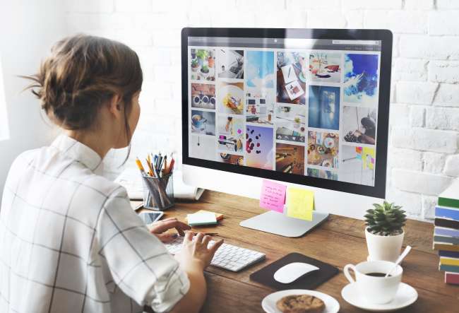 Best photo management software: Girl sitting on desk organizing photos on a Mac computer​