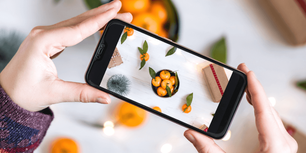 10 conseils de photographie iPhone pour des photos professionnelles - femme tenant un iphone prenant des photos d'oranges sur flatlay