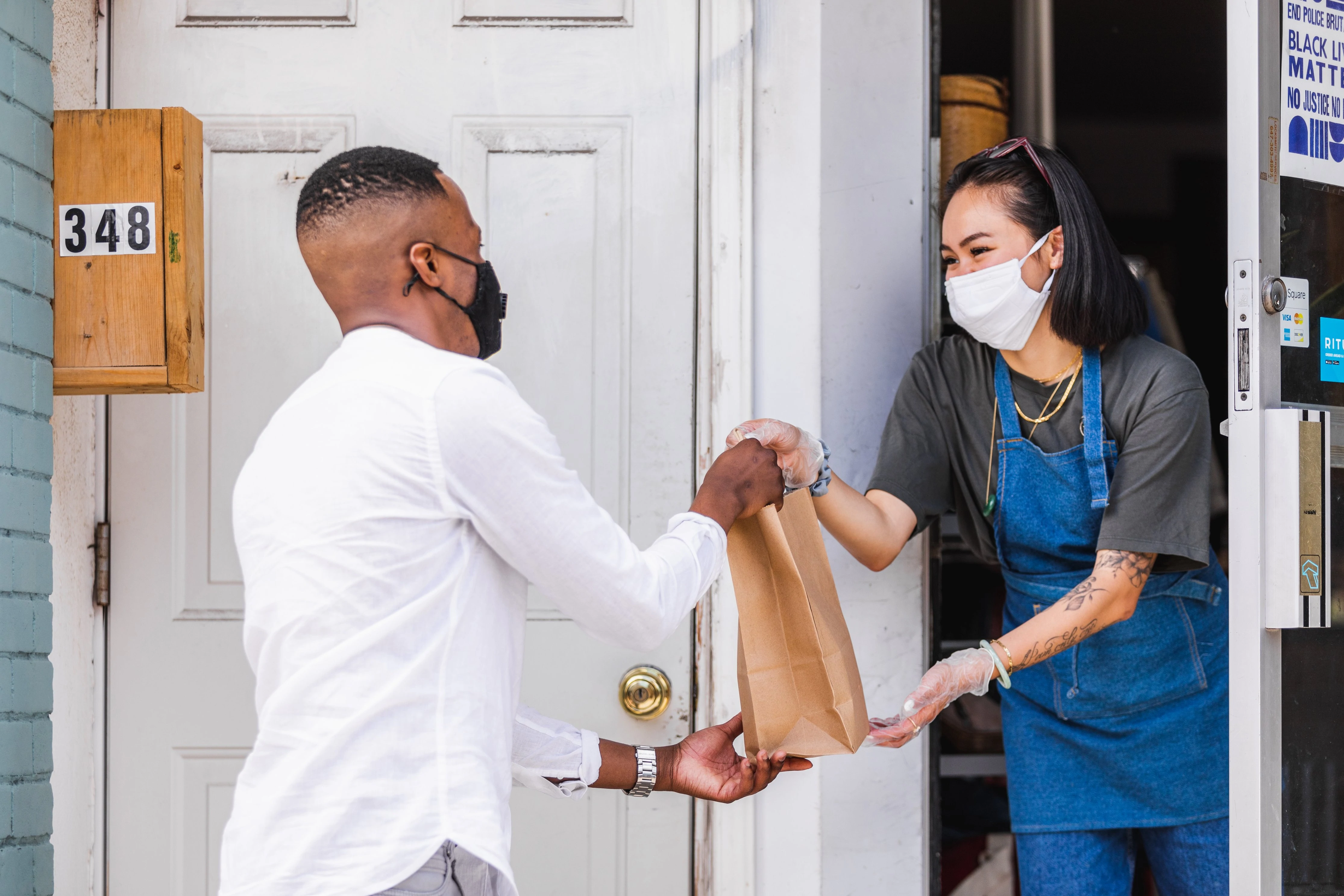 Un commerçant portant un masque passe un sac à un client par une porte