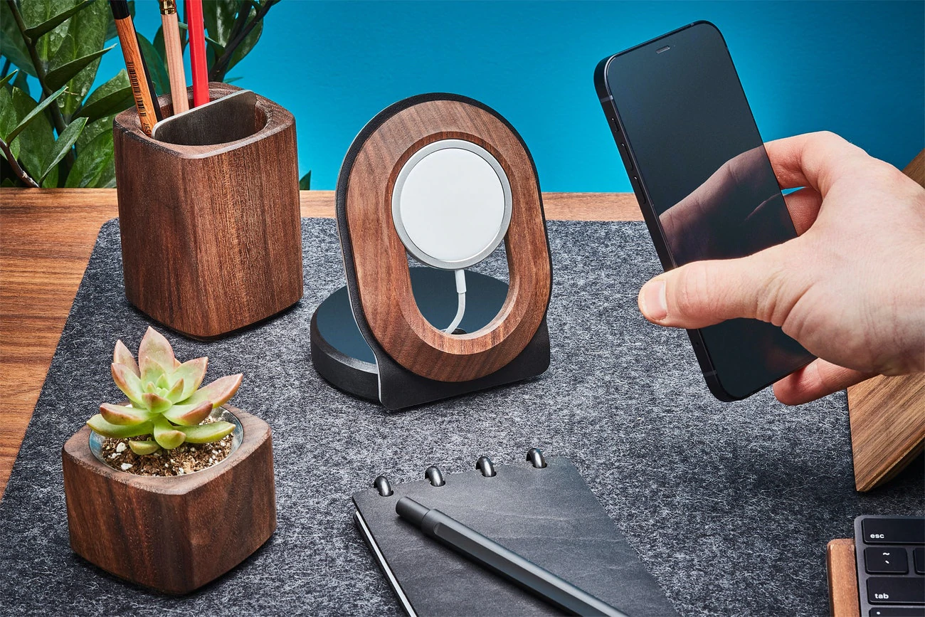 Une main tient un téléphone portable et des accessoires de bureau en bois et en laine sont assis sur un bureau en bois