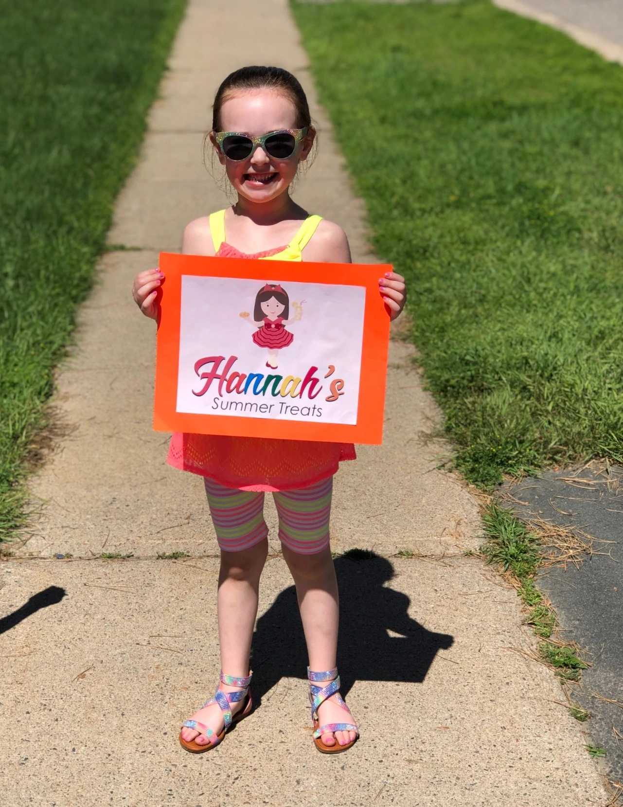 Hannah se tient sur le trottoir avec une pancarte promotionnelle pour Hannah's Treats.