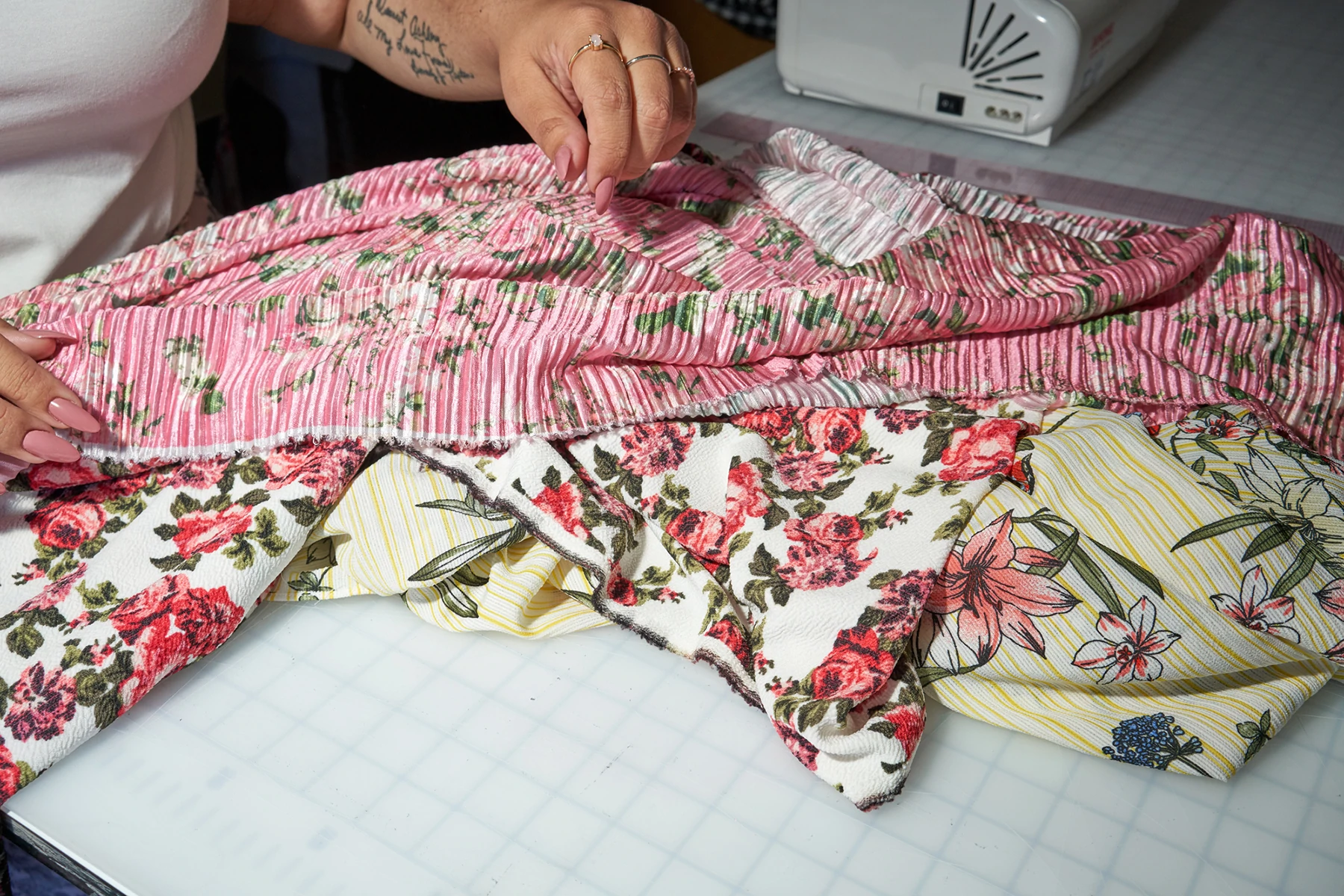 Gros plan sur les mains de la créatrice de mode Ashley Nell Tipton, travaillant avec un tissu rose à fleurs.