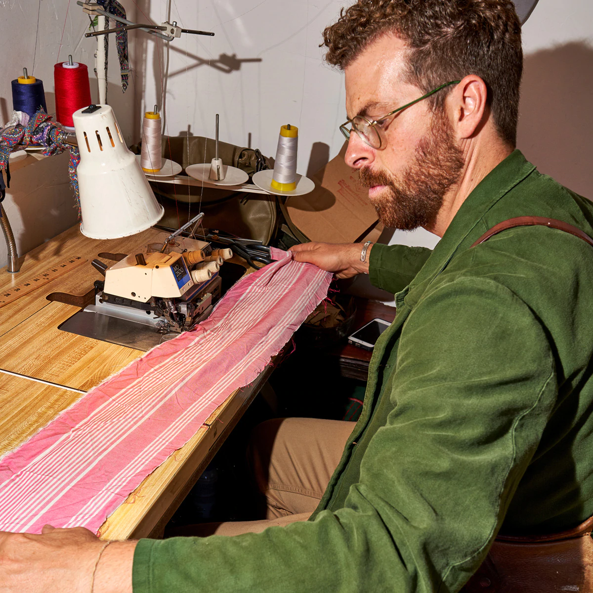 Matthew Schildkretr, fondatore di Late Sunday Afternoon a Venice, California, seduto al suo banco da lavoro con una striscia di tessuto rosa.