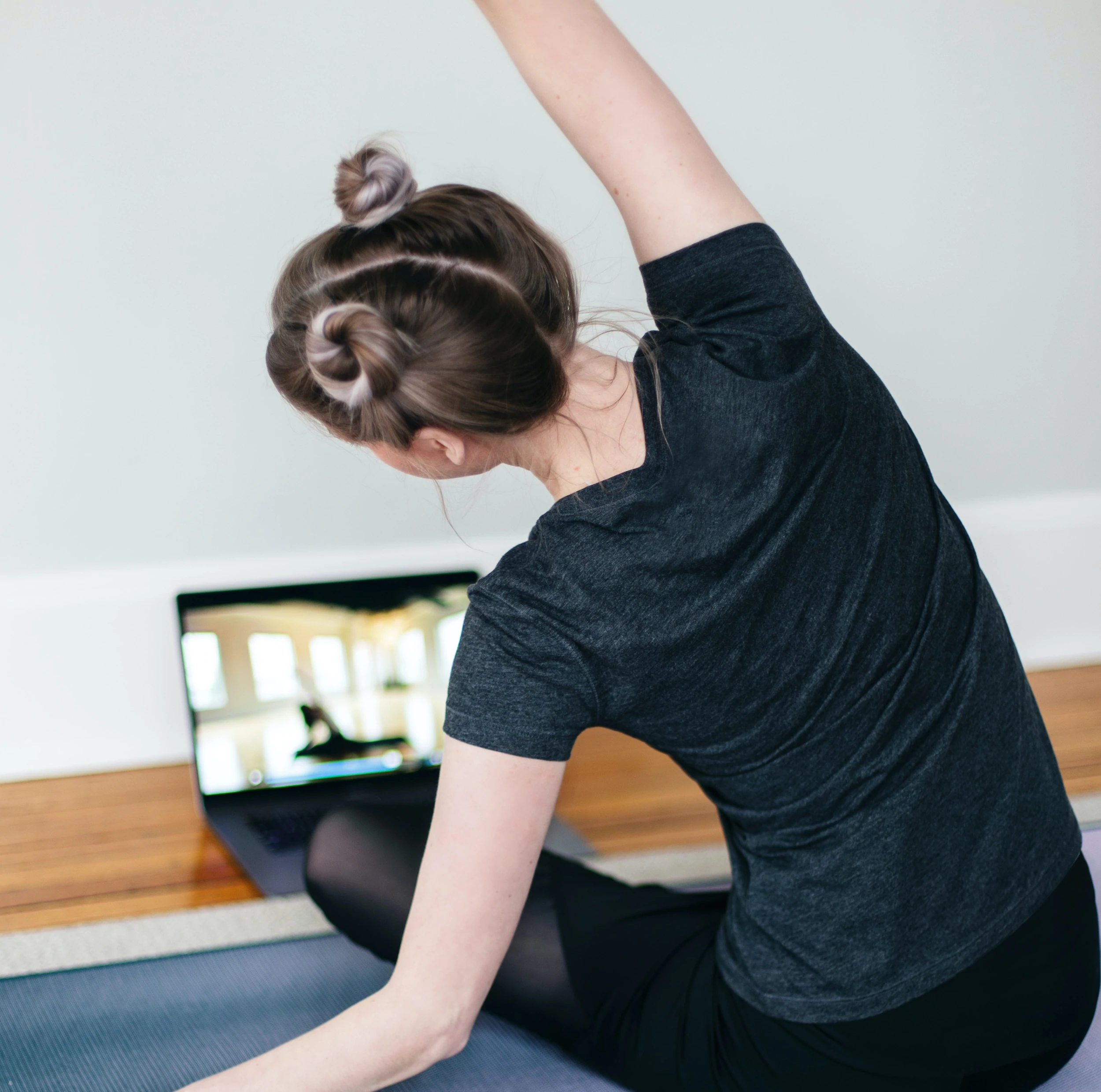 Une personne est assise sur un tapis de yoga et regarde un cours de yoga en direct sur un ordinateur portable