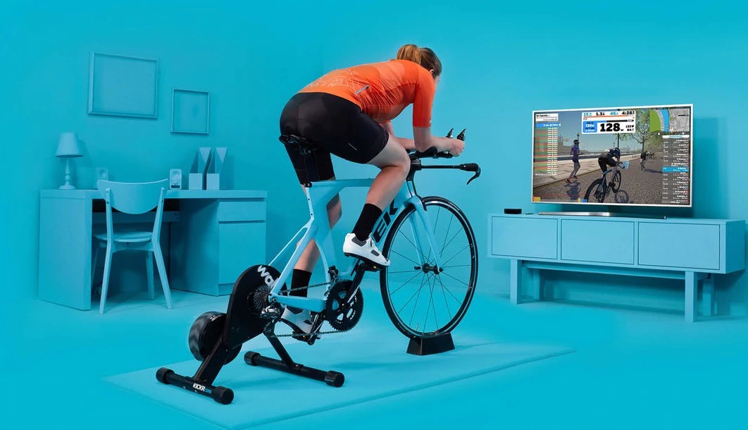 Un cycliste roule sur un vélo avec un entraîneur tout en participant à un circuit Zwift diffusé sur un téléviseur