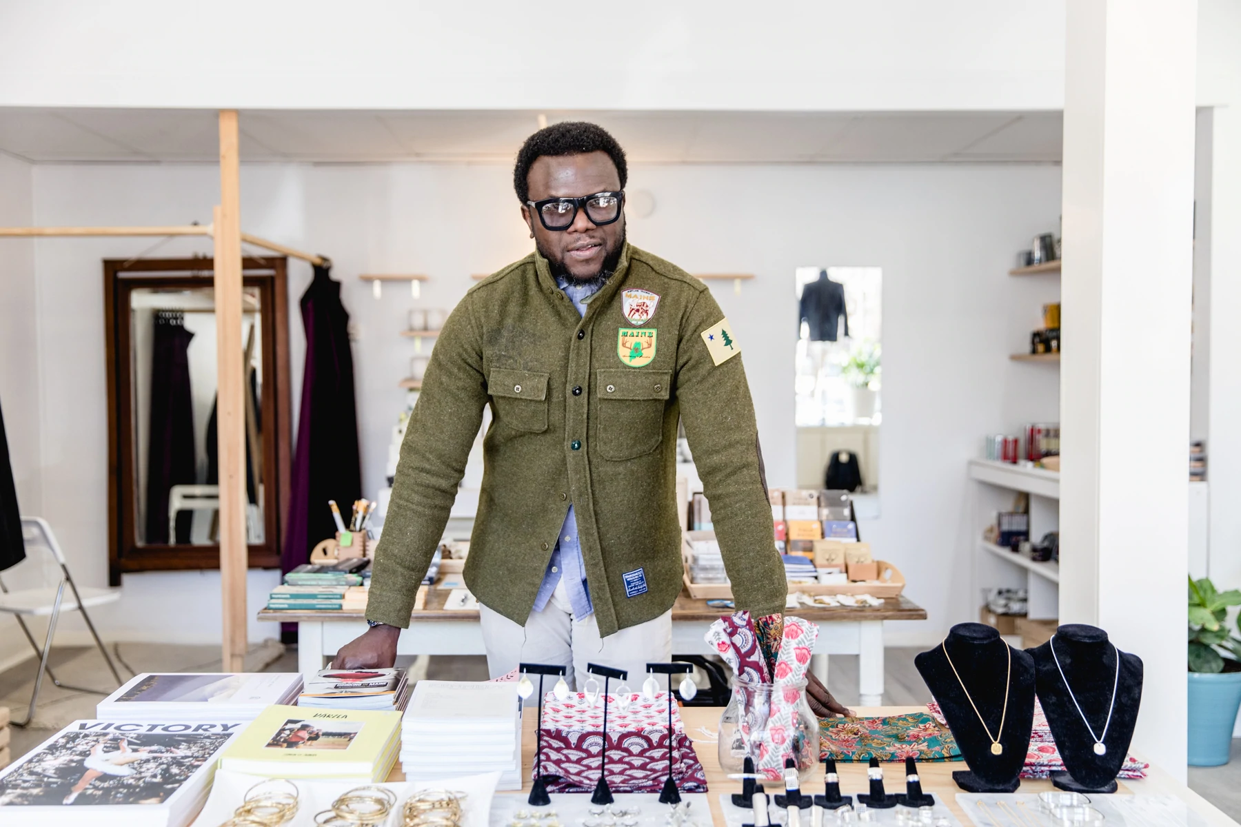 Le fondateur de Portland Trading Co., Kazeem Lawal, s'appuie sur une table d'exposition couverte de livres, de bijoux et de produits de style de vie.