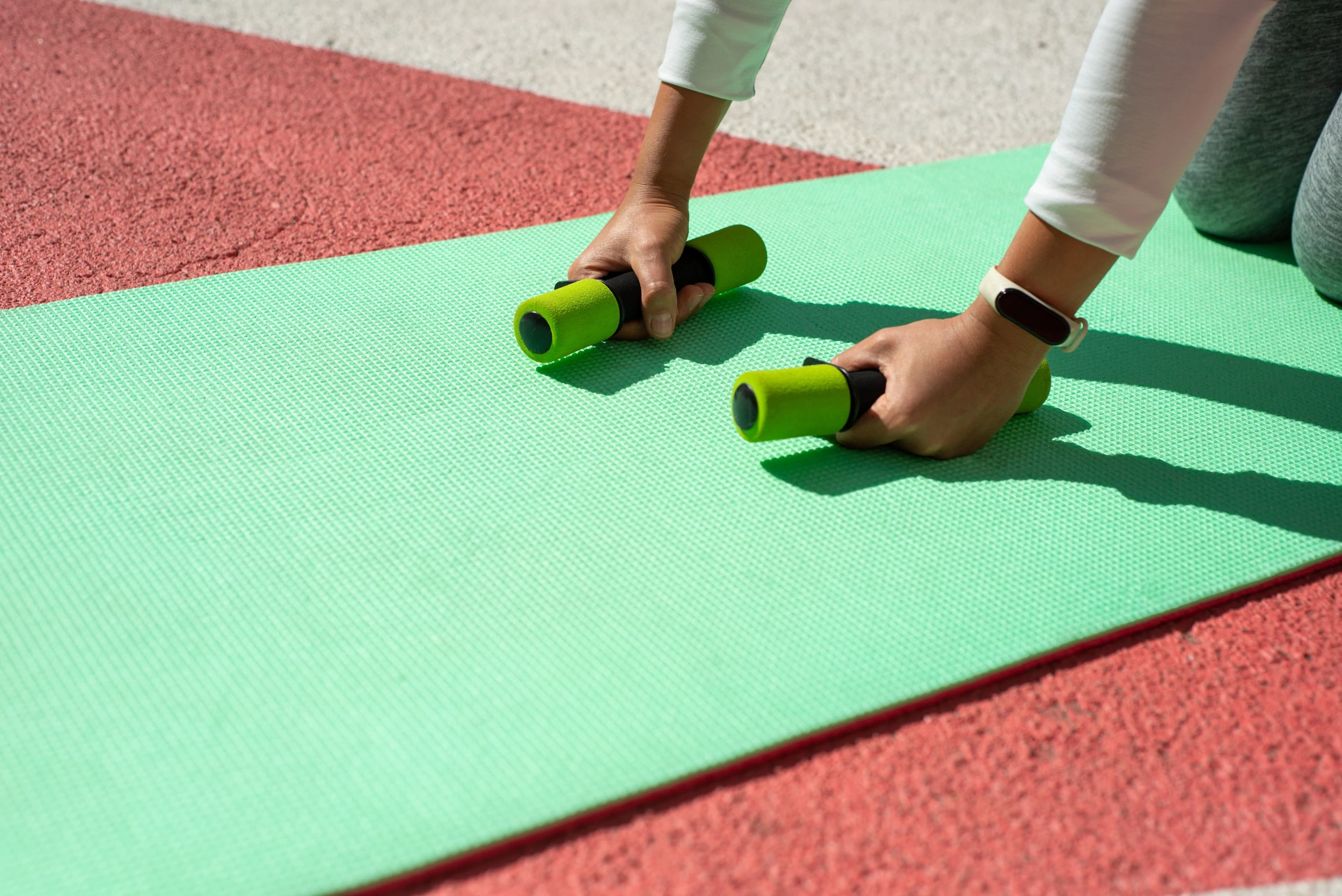 Dwie ręce trzymają ciężarki fitness na zielonej macie do jogi