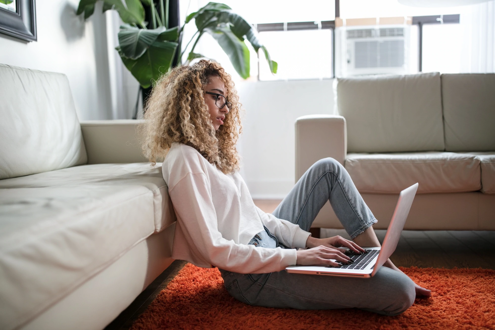 Une personne est assise par terre dans un salon et travaille sur un ordinateur portable