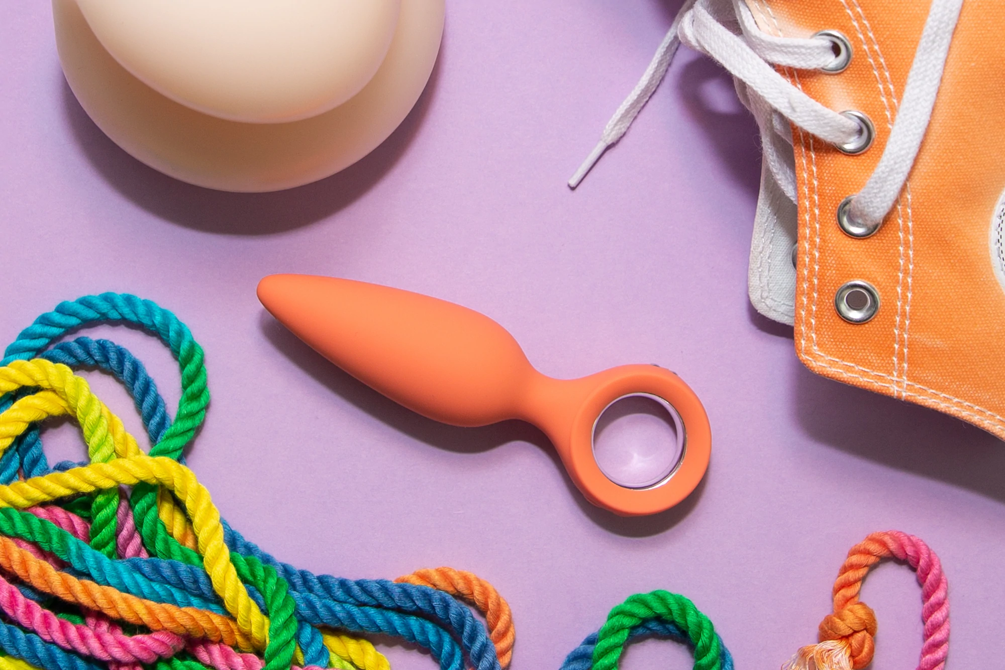 Flatlay de plusieurs objets, y compris un jouet sexuel orange, une sneaker orange et une corde arc-en-ciel