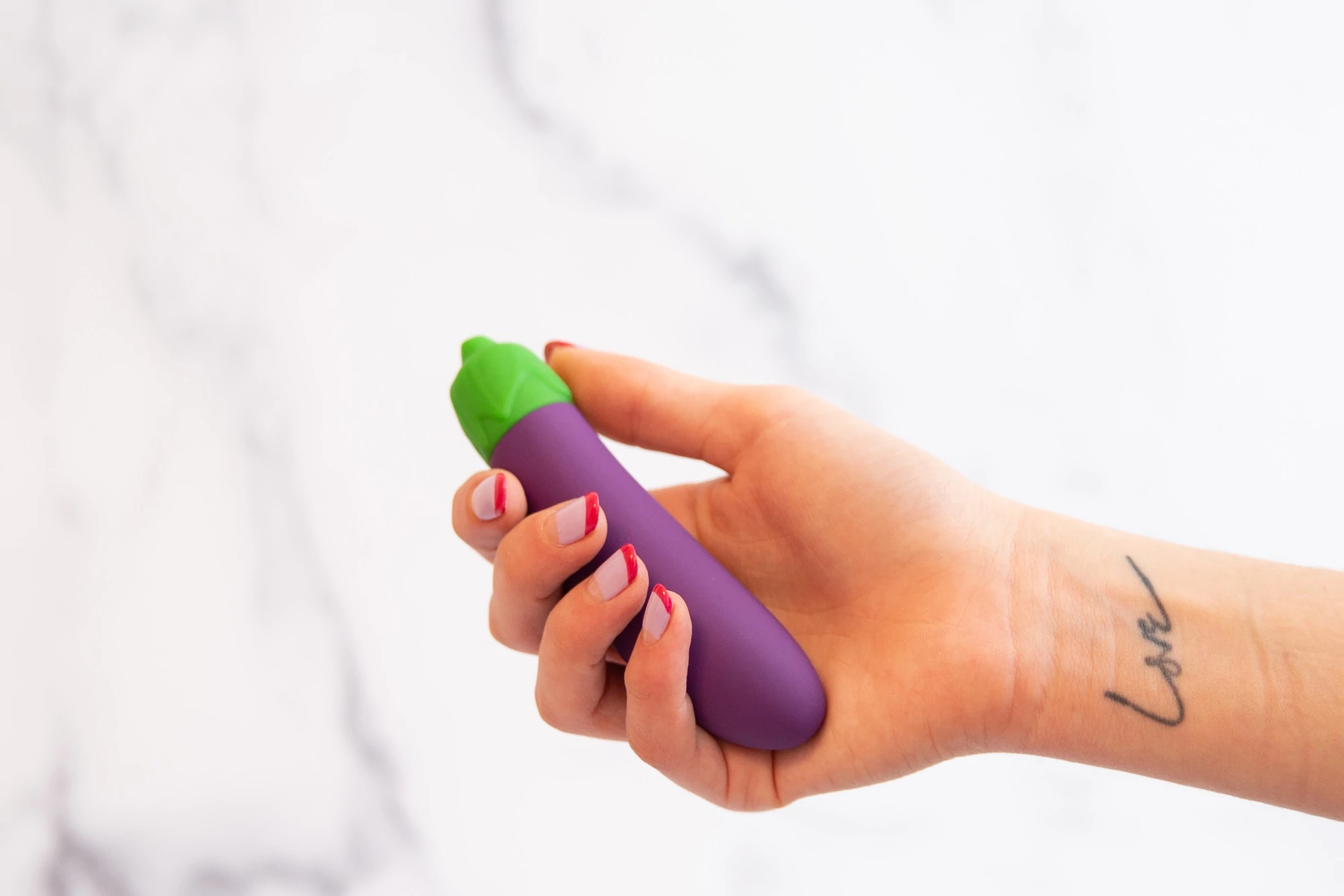 Une main tient un vibromasseur en forme d'aubergine