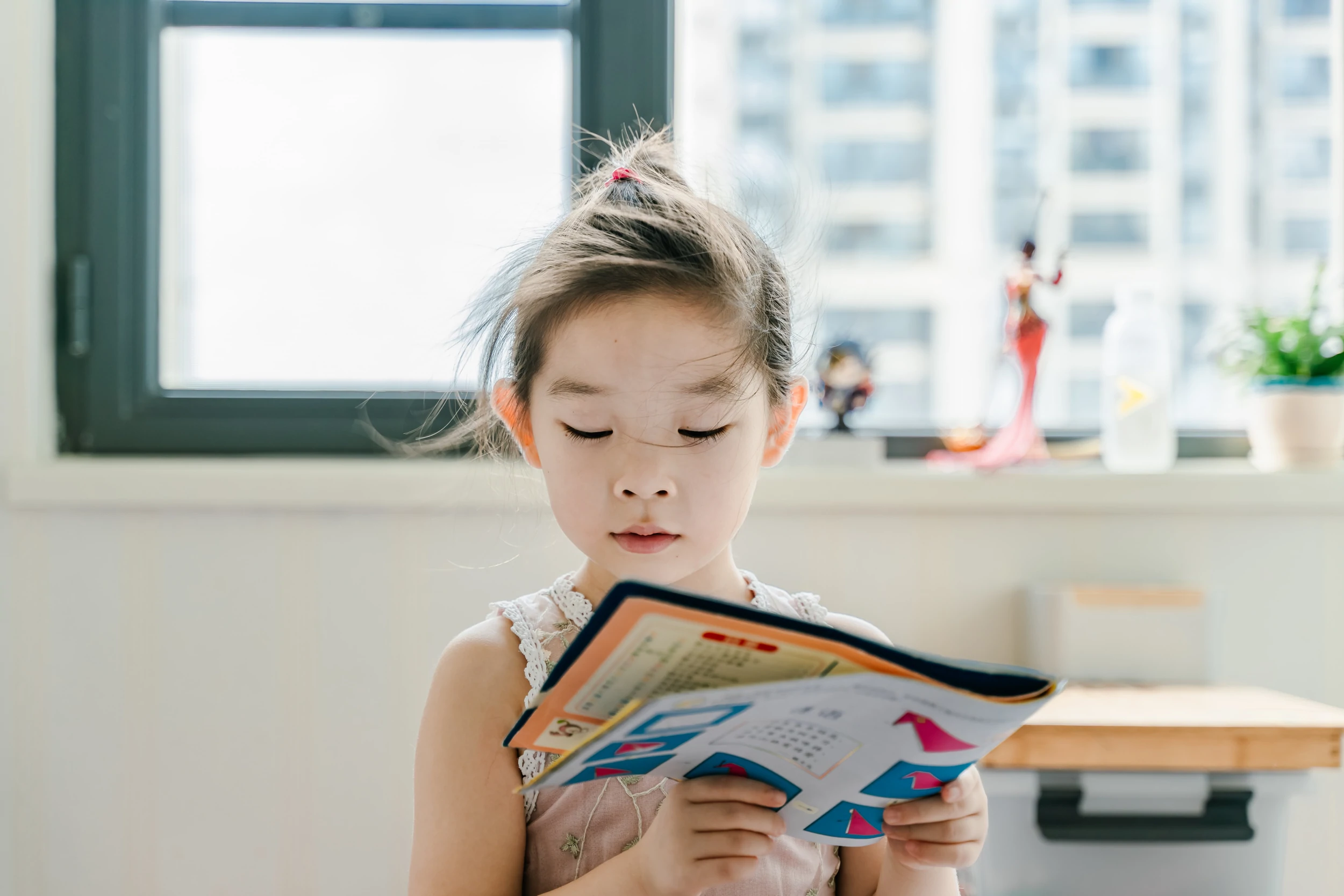 Un jeune enfant lit un livre devant une fenêtre