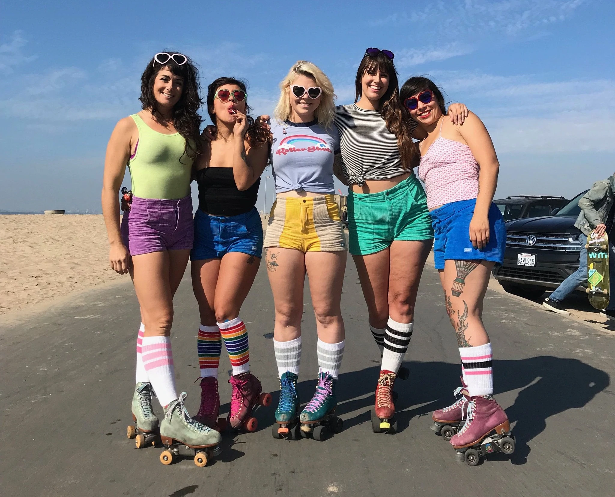 Retrato de cinco mulheres vestindo shorts e patins multicoloridos em um caminho de praia