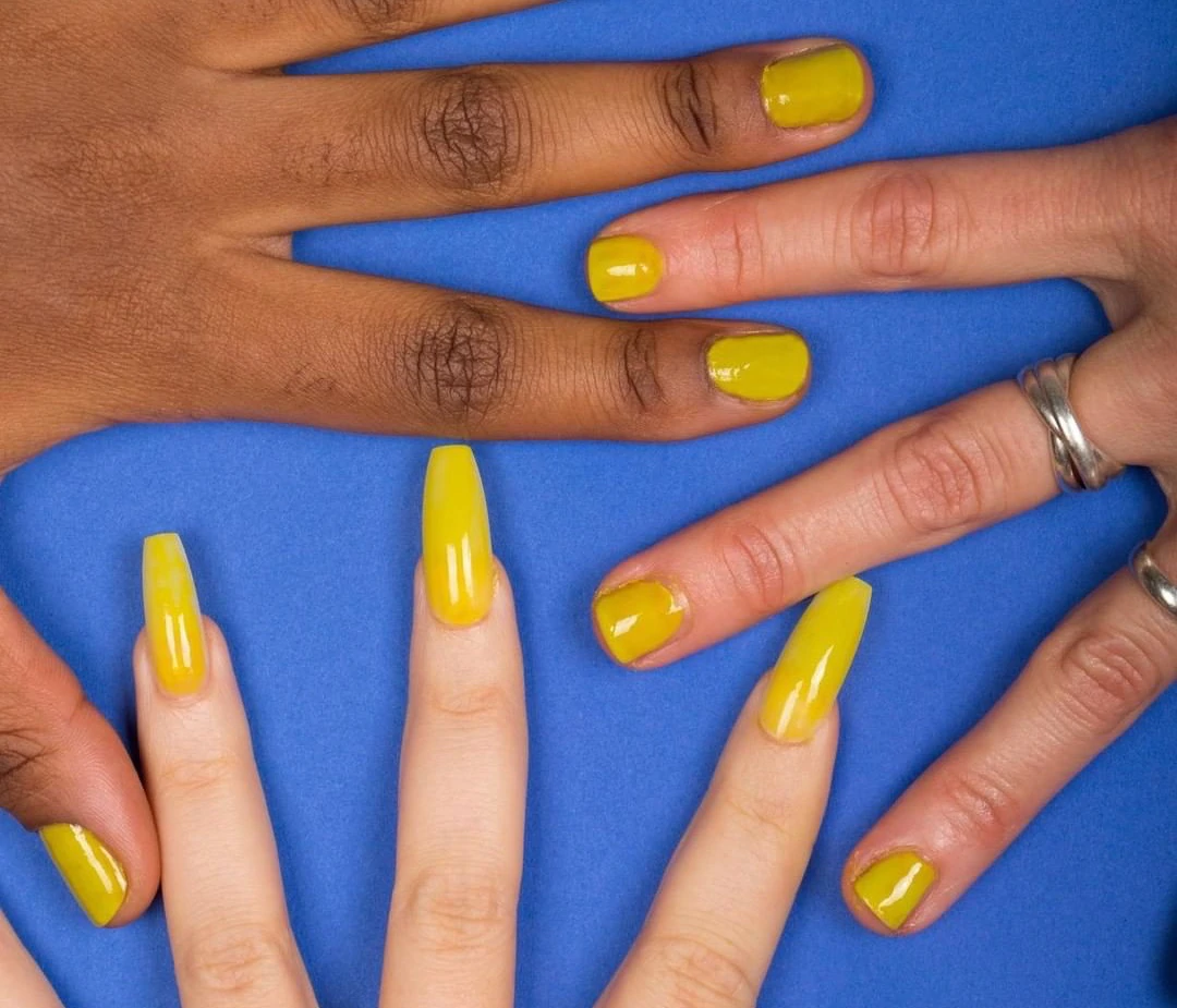 Esmalte amarelo fluido modelado em 3 mãos contra um fundo azul