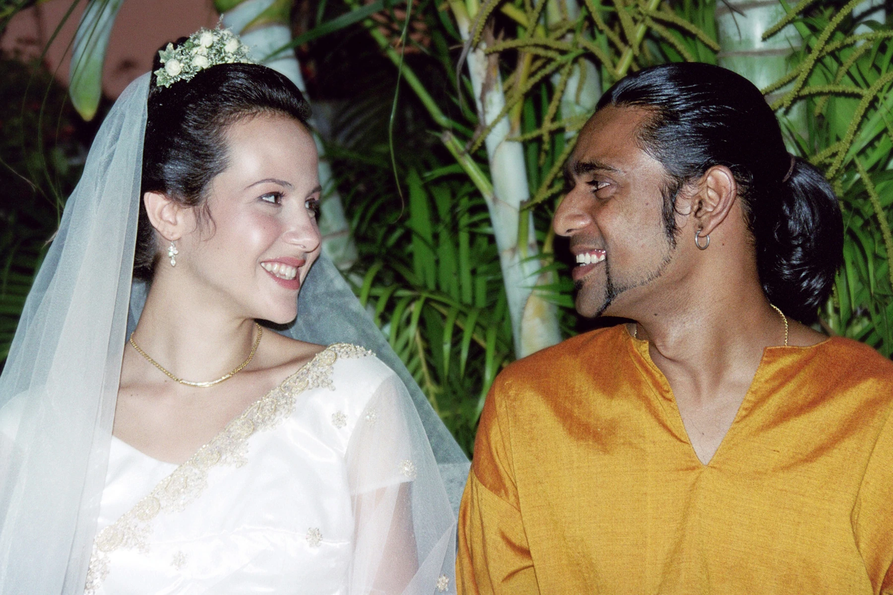 Retrato de casamento dos fundadores da Chas Organics, Marise May e Chanaka Kurera. Marise está usando um vestido de casamento tradicional ocidental e Chanaka está vestindo um saree laranja.