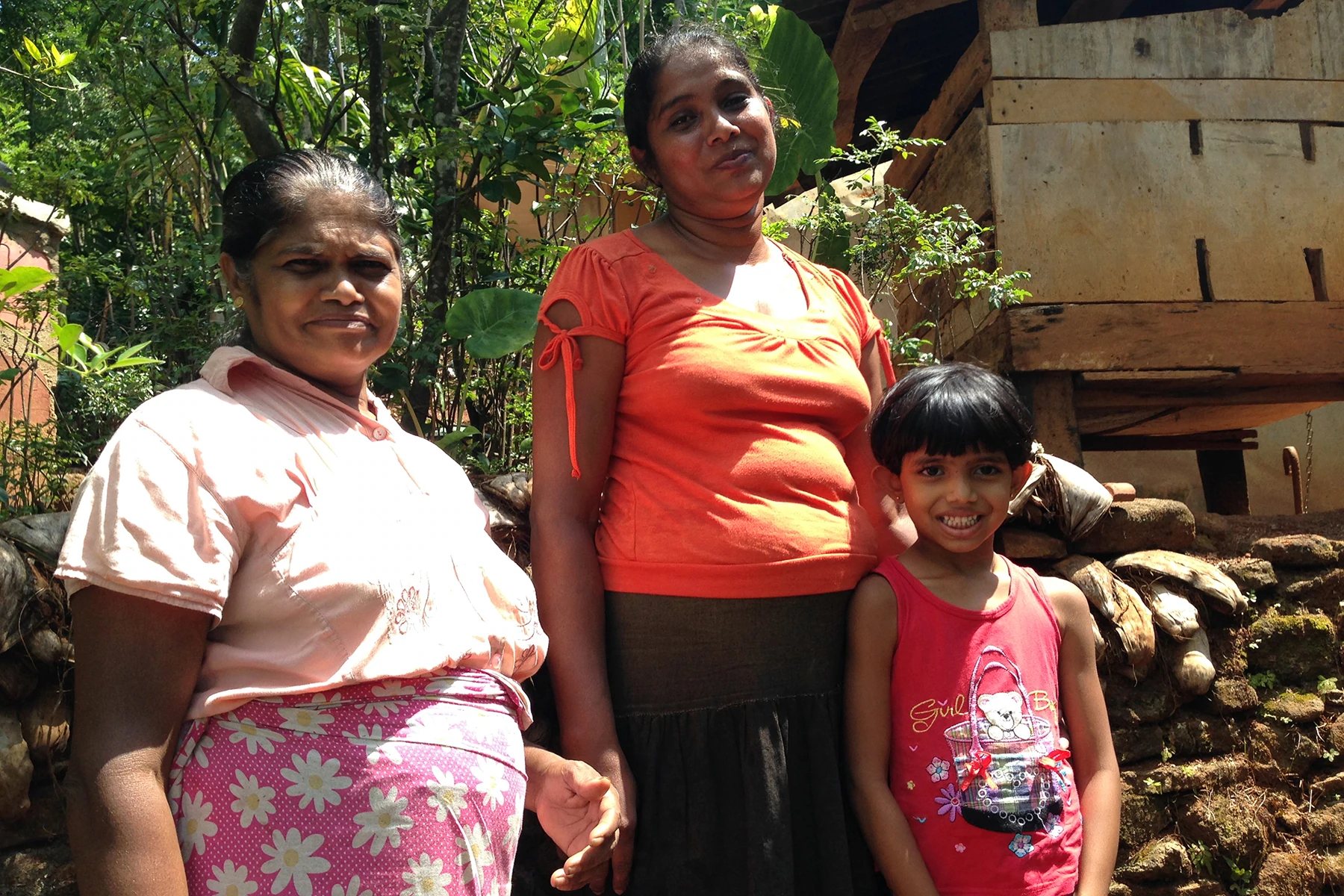 Fotografia de duas agricultoras orgânicas no Sri Lanka em pé com uma jovem entre 7 e 9 anos de idade.