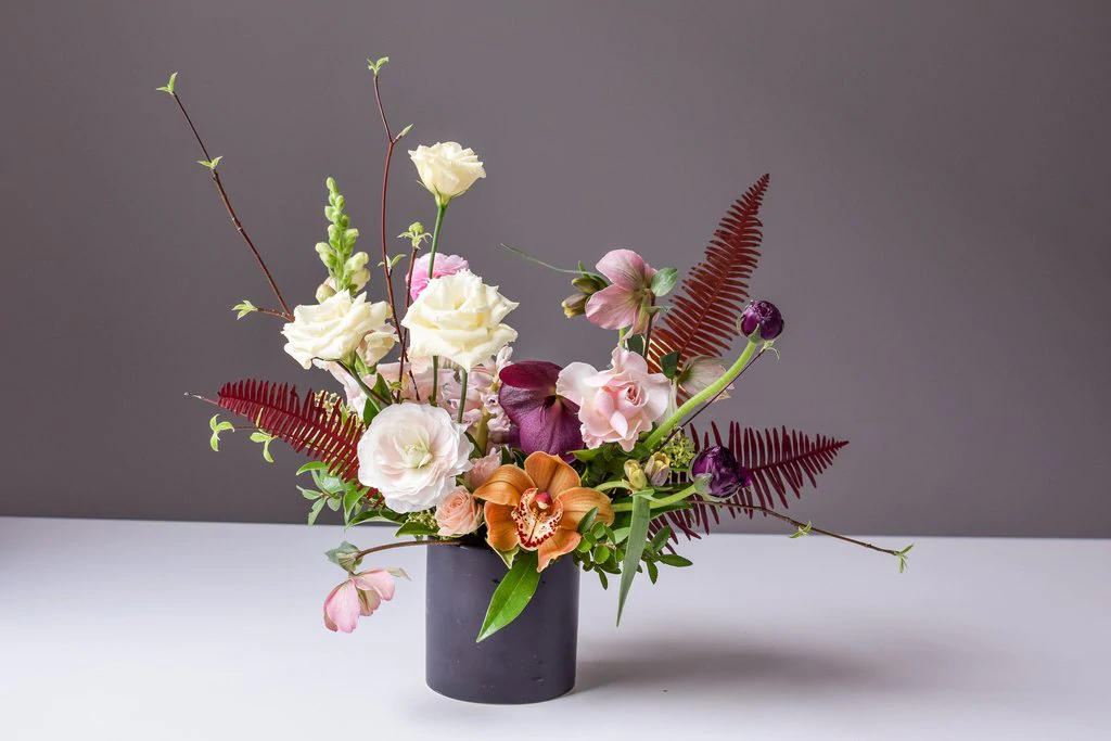 Un vase gris rempli d'un bouquet de fleurs est posé sur une surface sur un fond uni