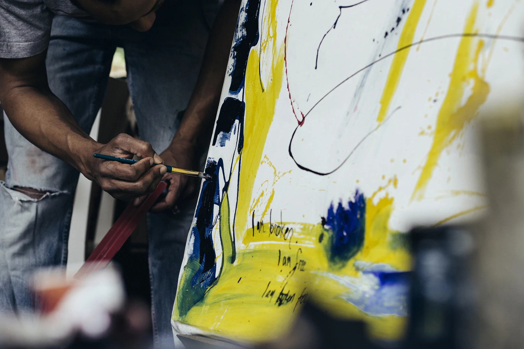 Dentro do estúdio de um pintor, uma mão segura um pincel e faz traços em uma tela