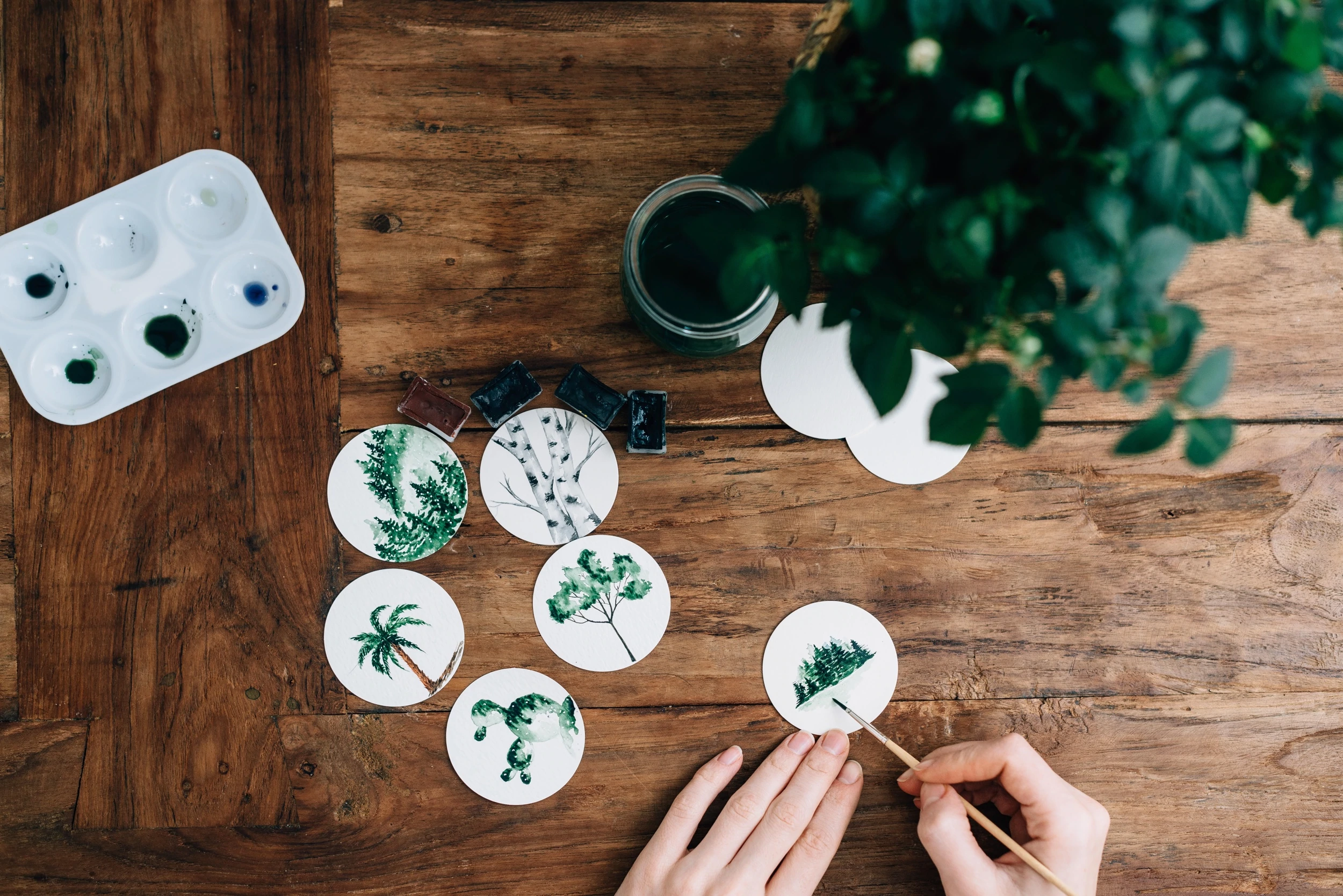 Mãos pintam delicadas folhas de aquarela em pequenos círculos de papel