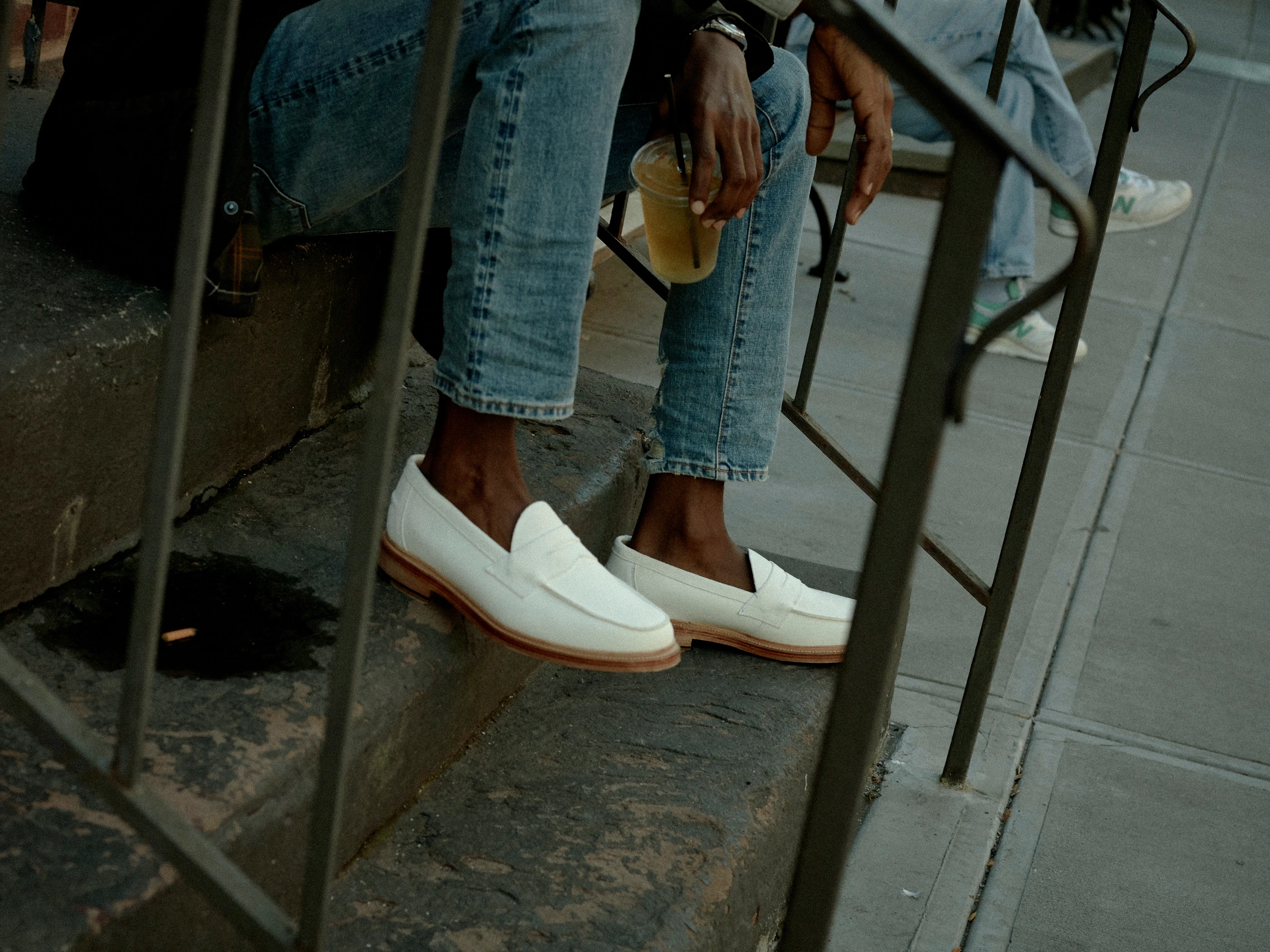 Foto próxima abaixo dos joelhos de uma pessoa vestindo jeans e mocassins brancos