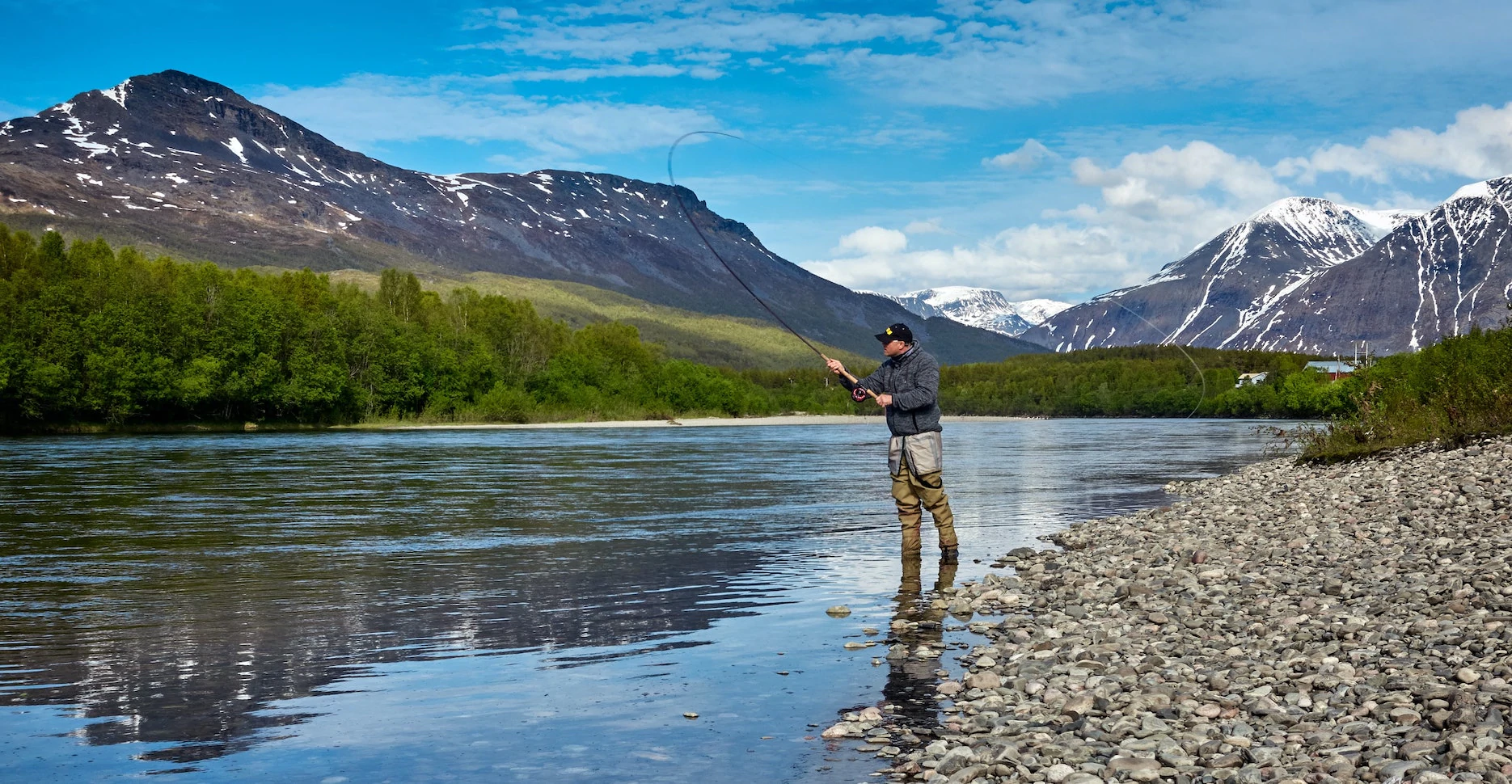 Uma imagem de um homem pescando em uma lagoa em frente às montanhas