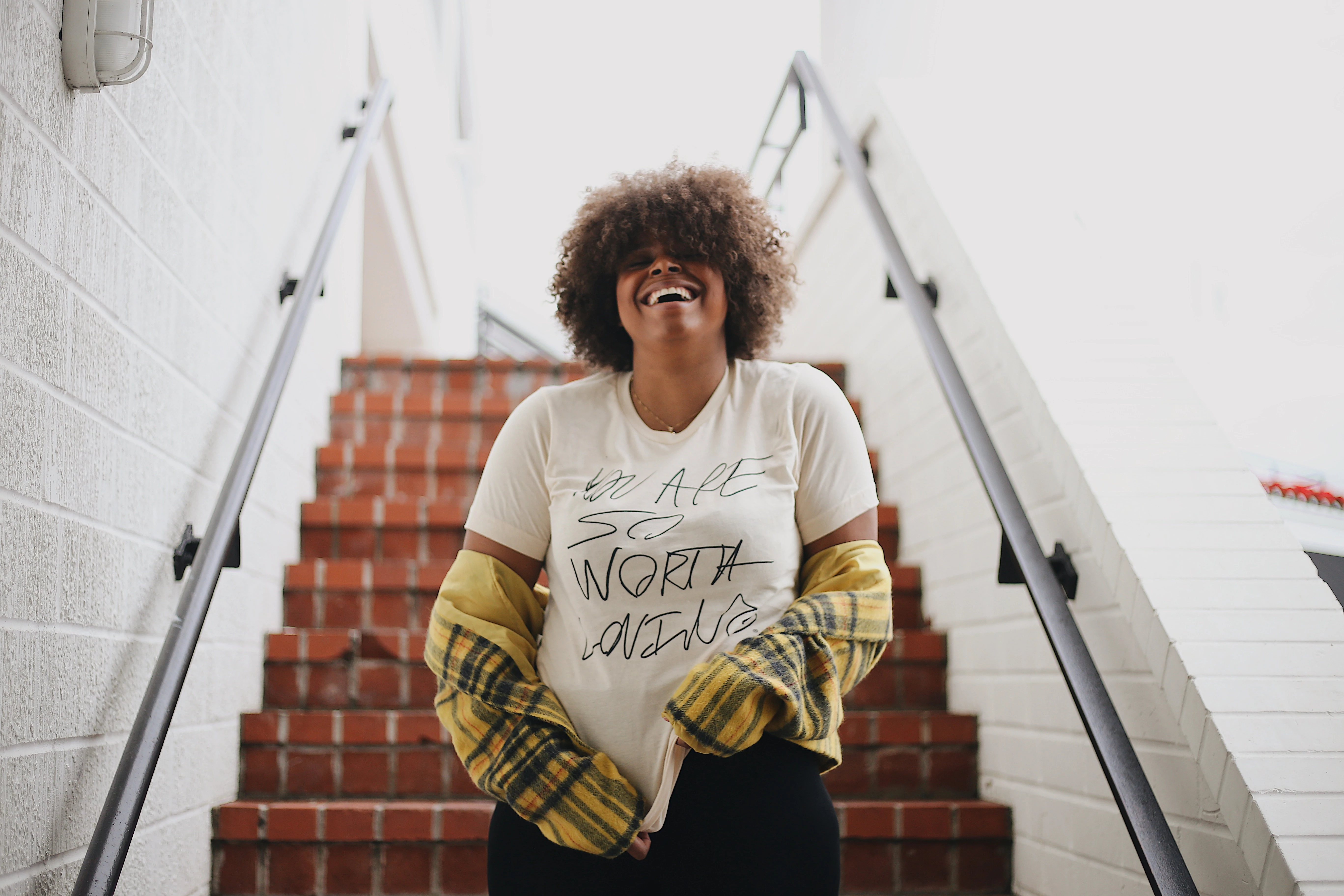 Una modelo cerca de unas escaleras con una camiseta de So Worth Loving.