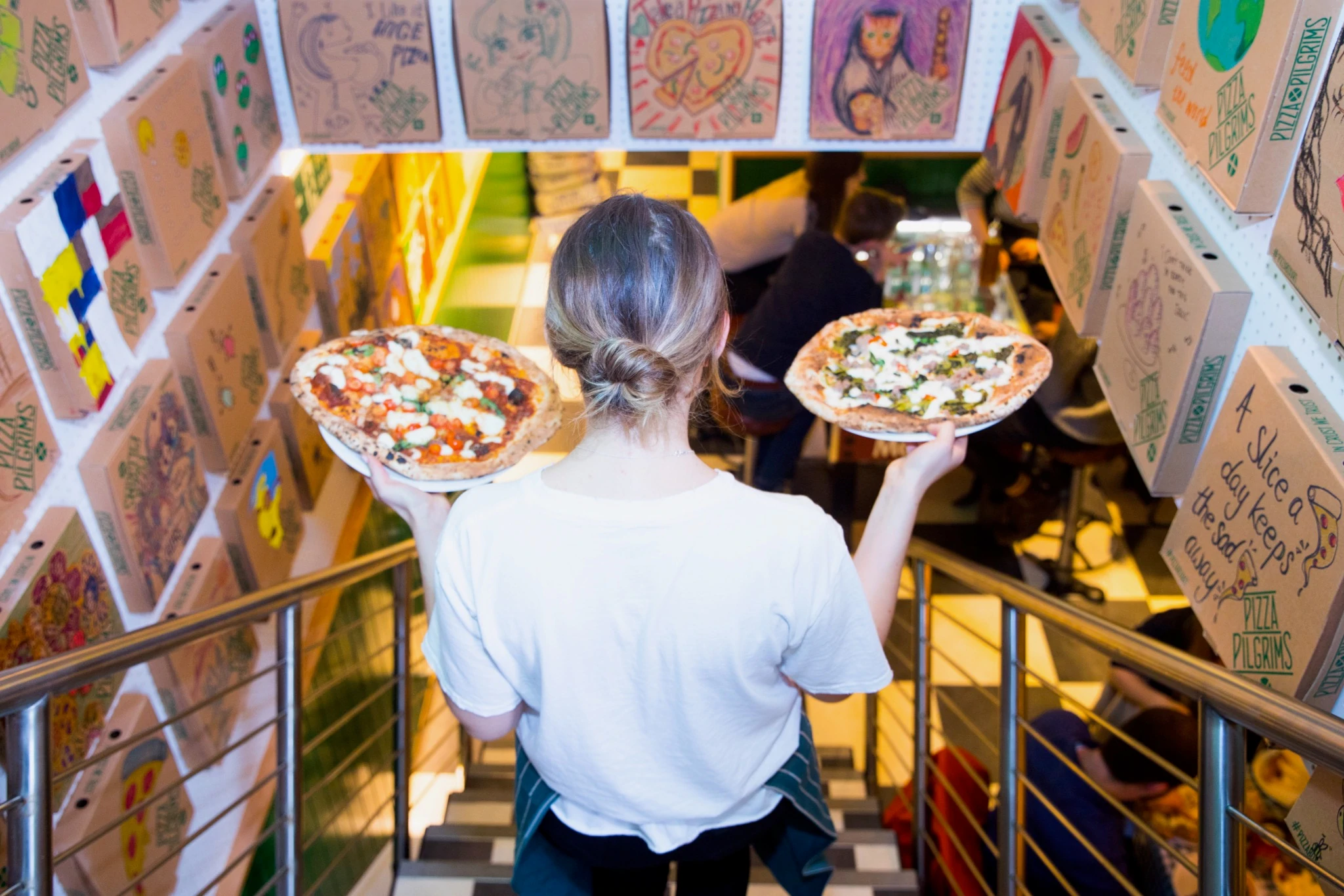 Una cameriera con due pizze in mano presso la sede di Shoreditch di Pizza Pilgrims ai suoi giorni frenetici prima del COVID-19