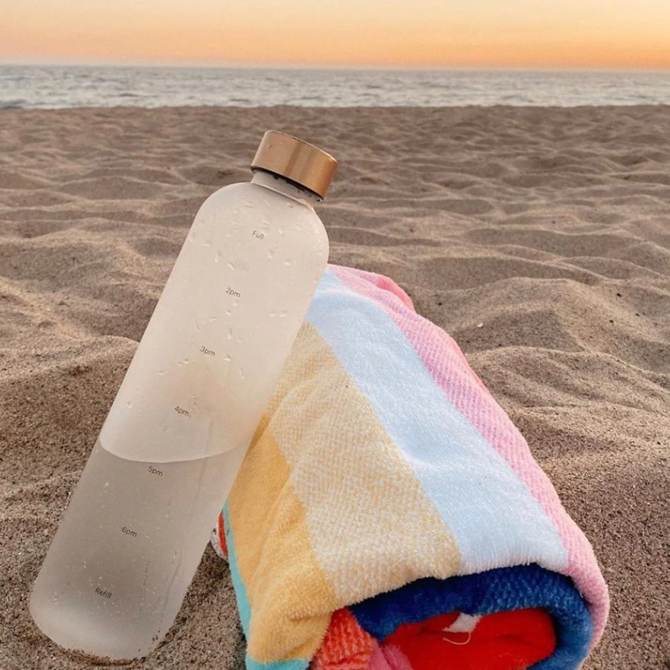 Una bottiglia d'acqua di Healthish sulla spiaggia accanto a un telo mare.