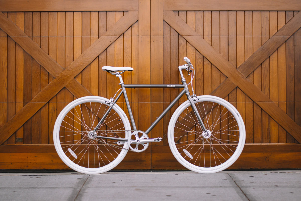 A bicycle by Brooklyn Bicycle Co. displayed against wooden doors and concrete floors.