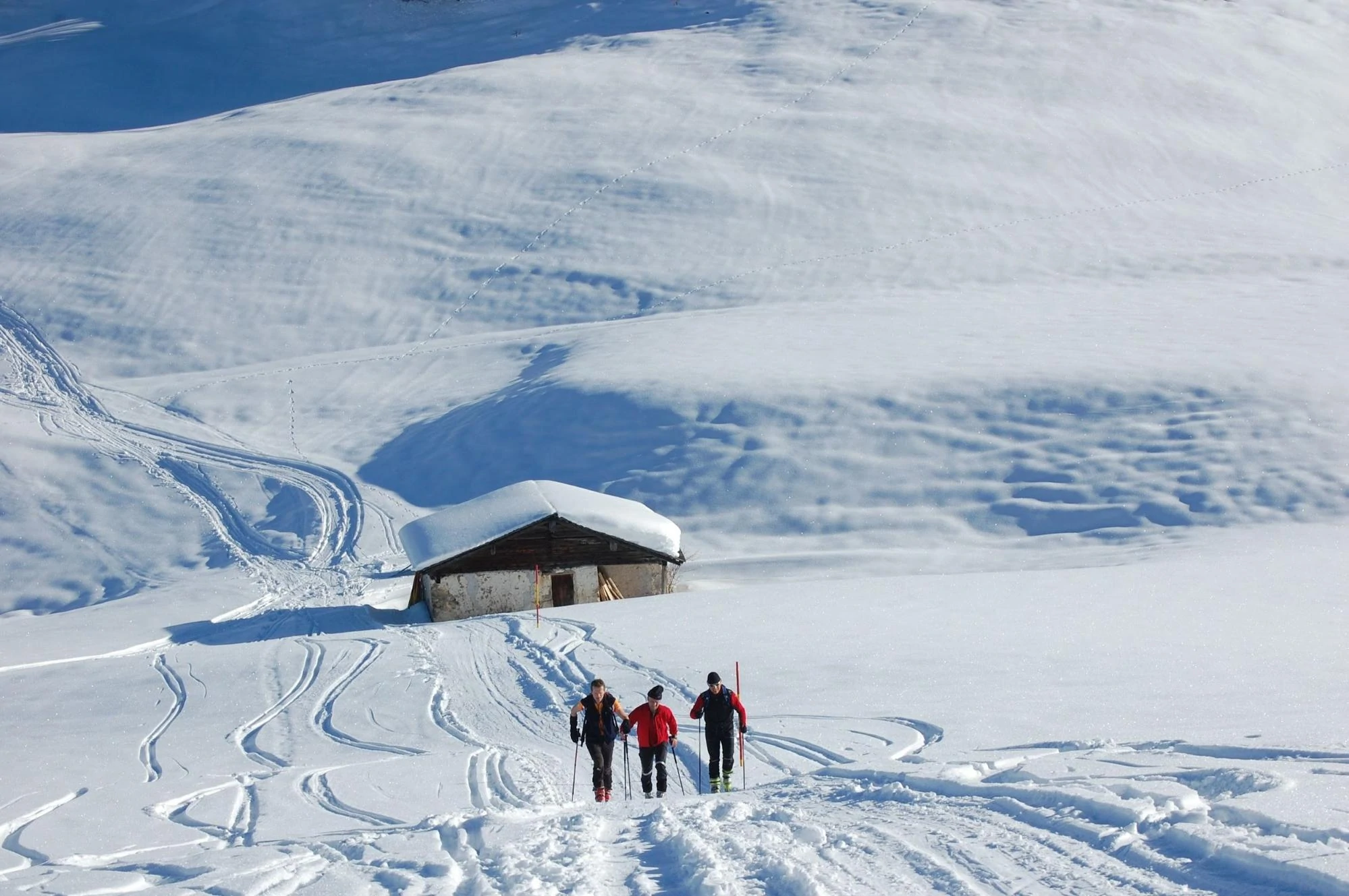 Un gruppo di tre sciatori che cammina nella neve sullo sfondo di uno chalet.