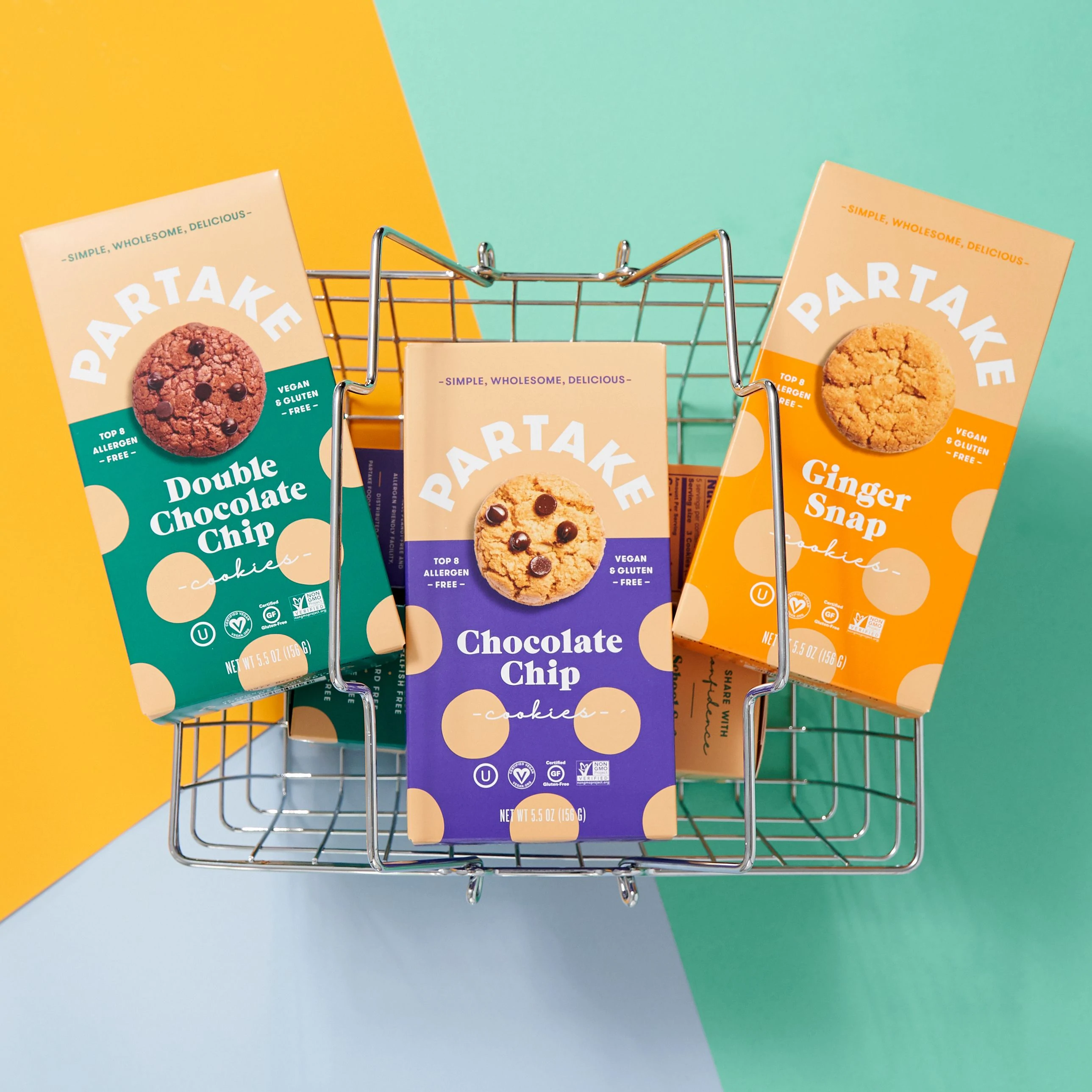 Trio kotak kue Parttake Foods dalam rasa Double Chocolate Chip, Chocolate Chip, dan Ginger Snap yang dilatarbelakangi oleh keranjang belanjaan logam.