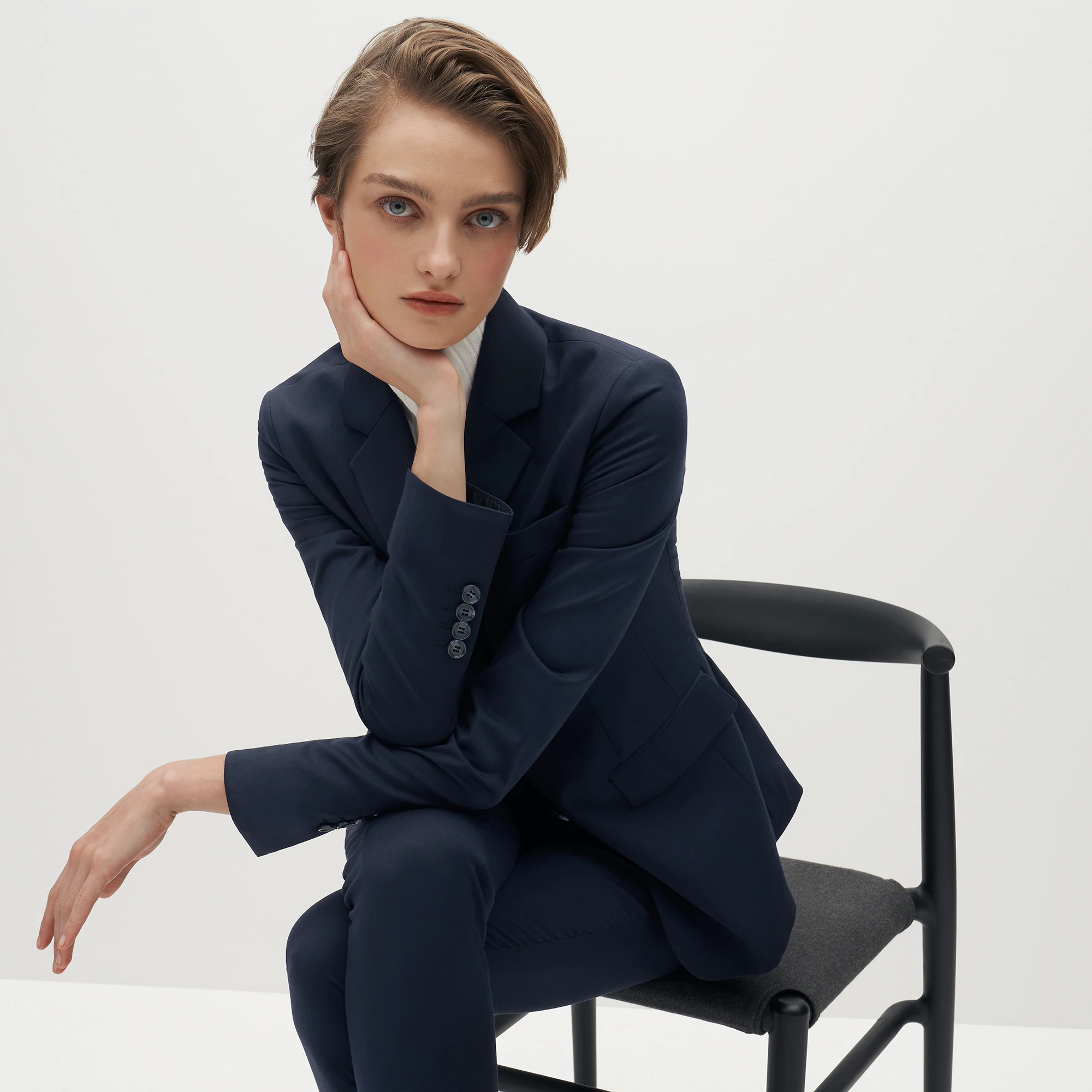 The Groomsman Suit: A female model wearing a navy suit sitting in a chair.