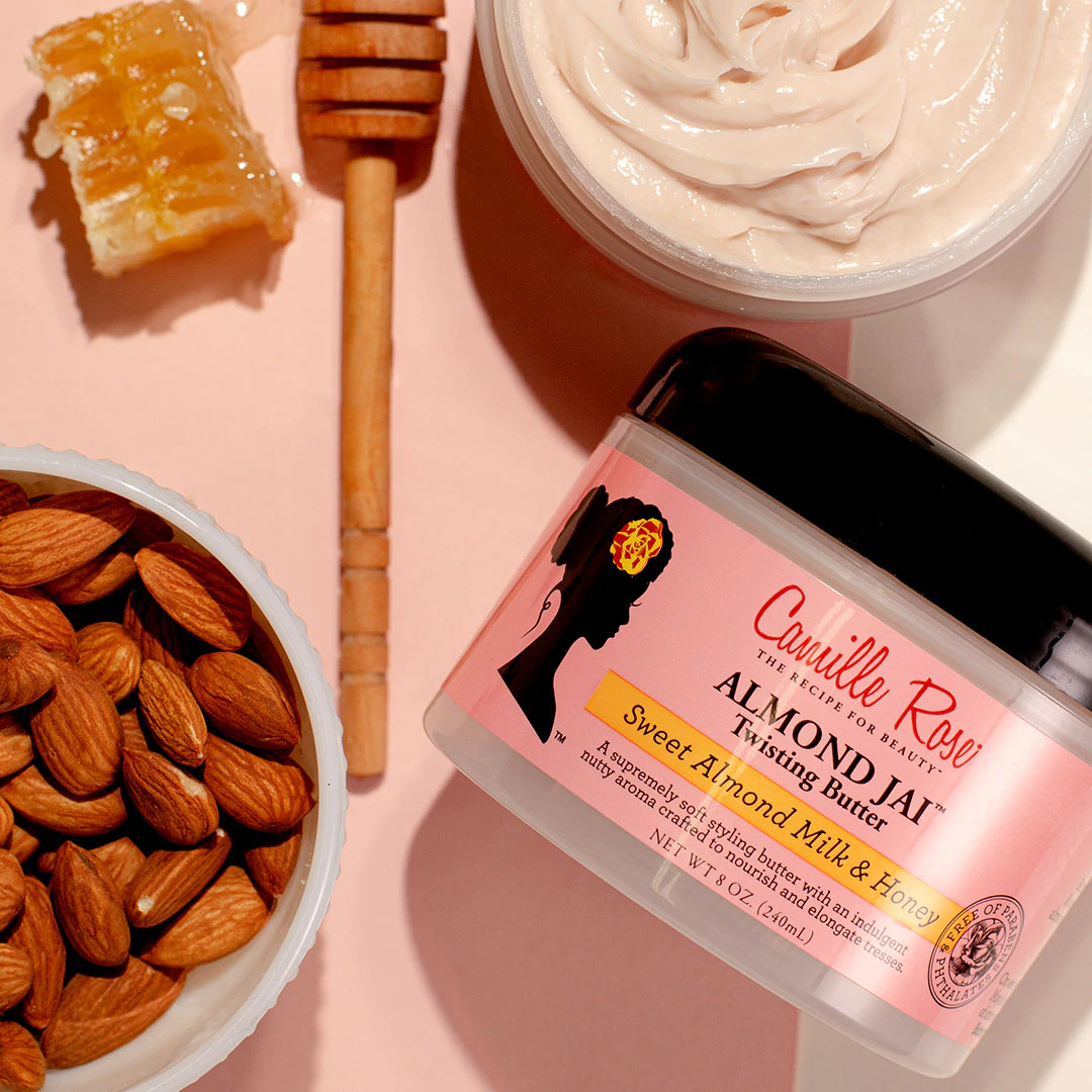 Un vasetto di Camille Rose Almond Jai Twisting Butter insieme a mandorle crude e favo.