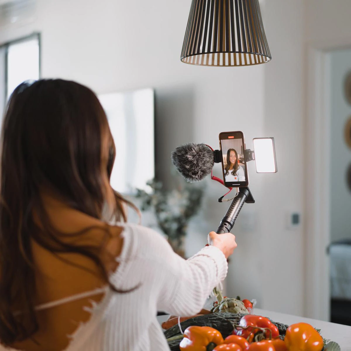 Una modella con autostick, smartphone e illuminazione Lume Cube che si registra in cucina.