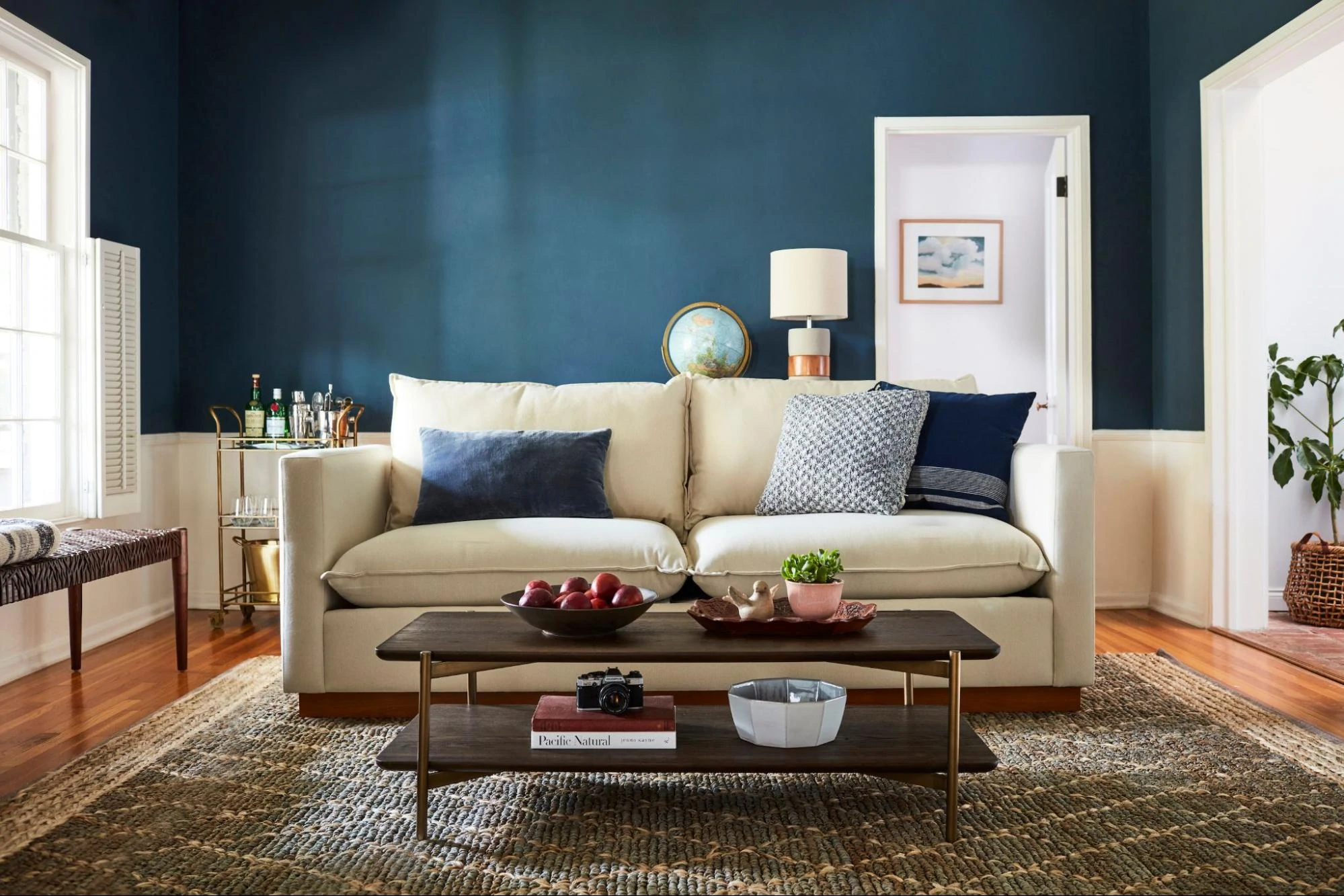 A white loveseat backdropped by a blue room complete with a coffee table and bar cart.