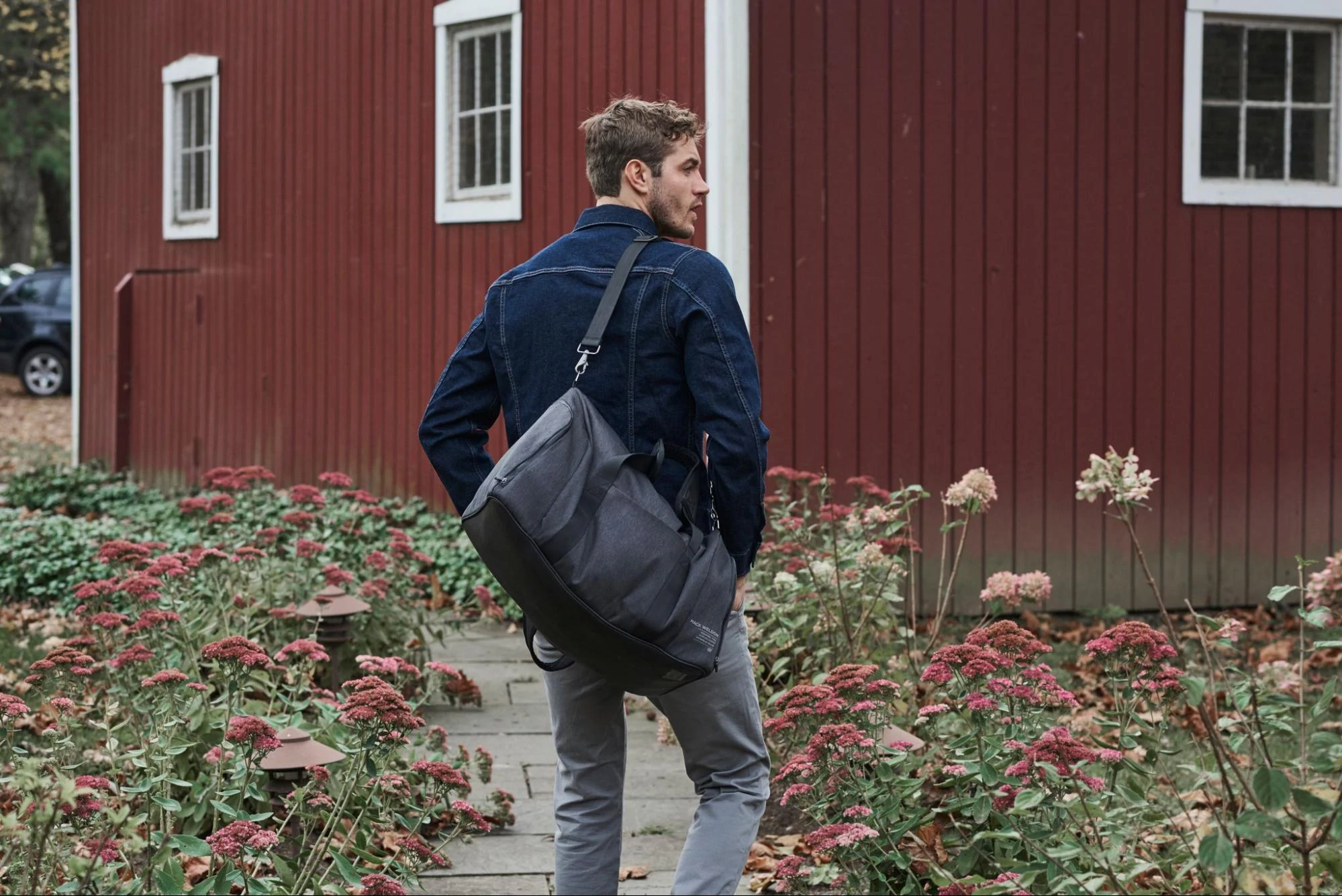 Ein Model in einer Jeansjacke und Jeans mit einer Weekender-Tasche von Mack Weldon.