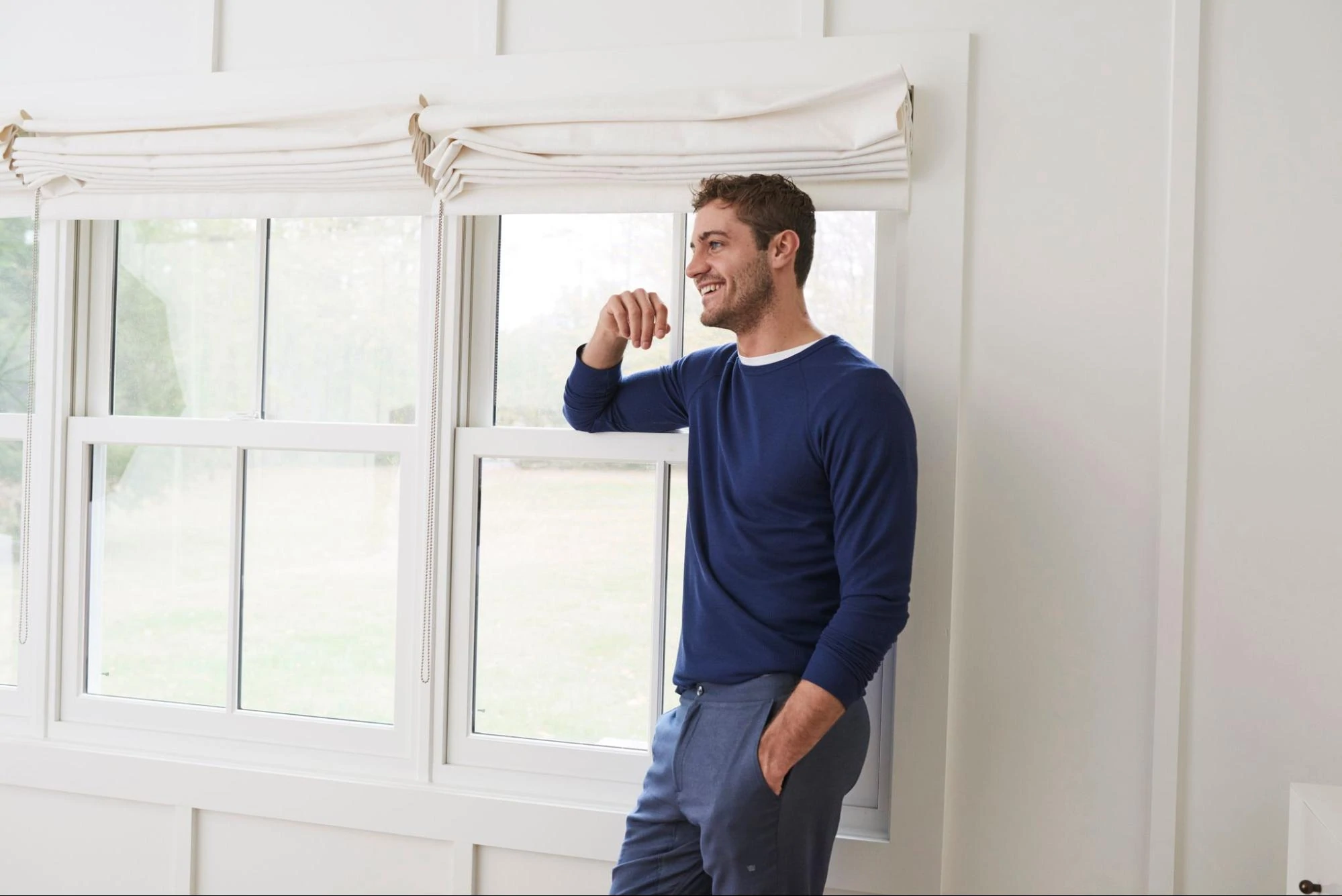 Ein Model, das einen blauen Pullover und eine Anzughose von Mack Weldon entwöhnt