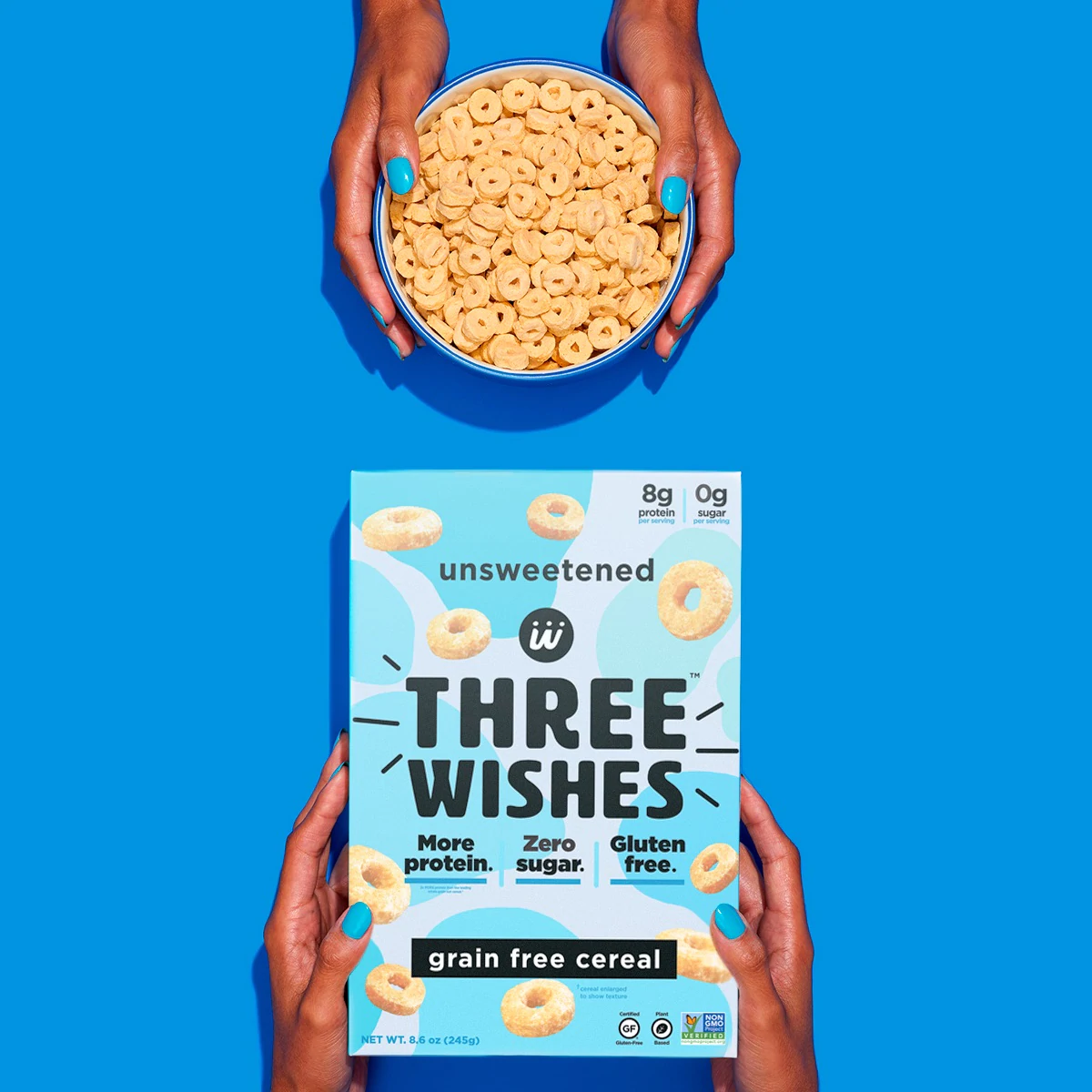 The unsweetened cereal by Three Wishes Creal held up by a pair of hands against a blue background.