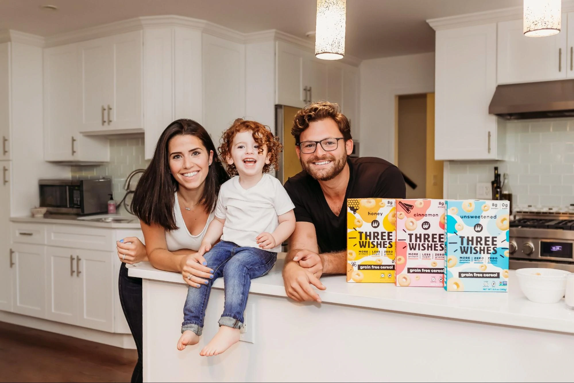 Margaret und Ian Wishingard zusammen mit ihrem Lied Ellis in einer Küche mit Schachteln von Three Wishes Cereal auf der Theke.