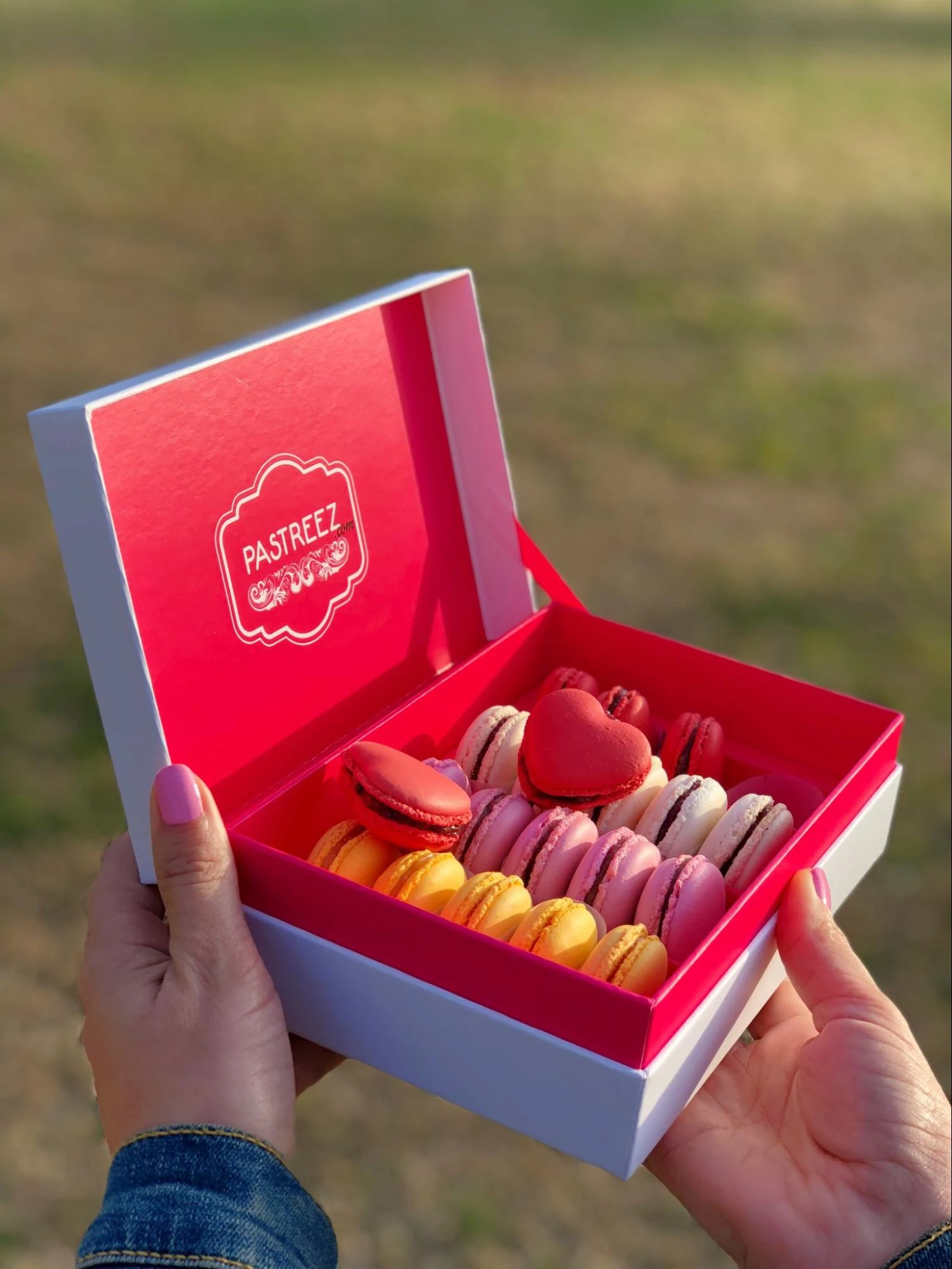 Sebuah kotak macarons berbentuk hati oleh Pastreez dipegang oleh model tangan.