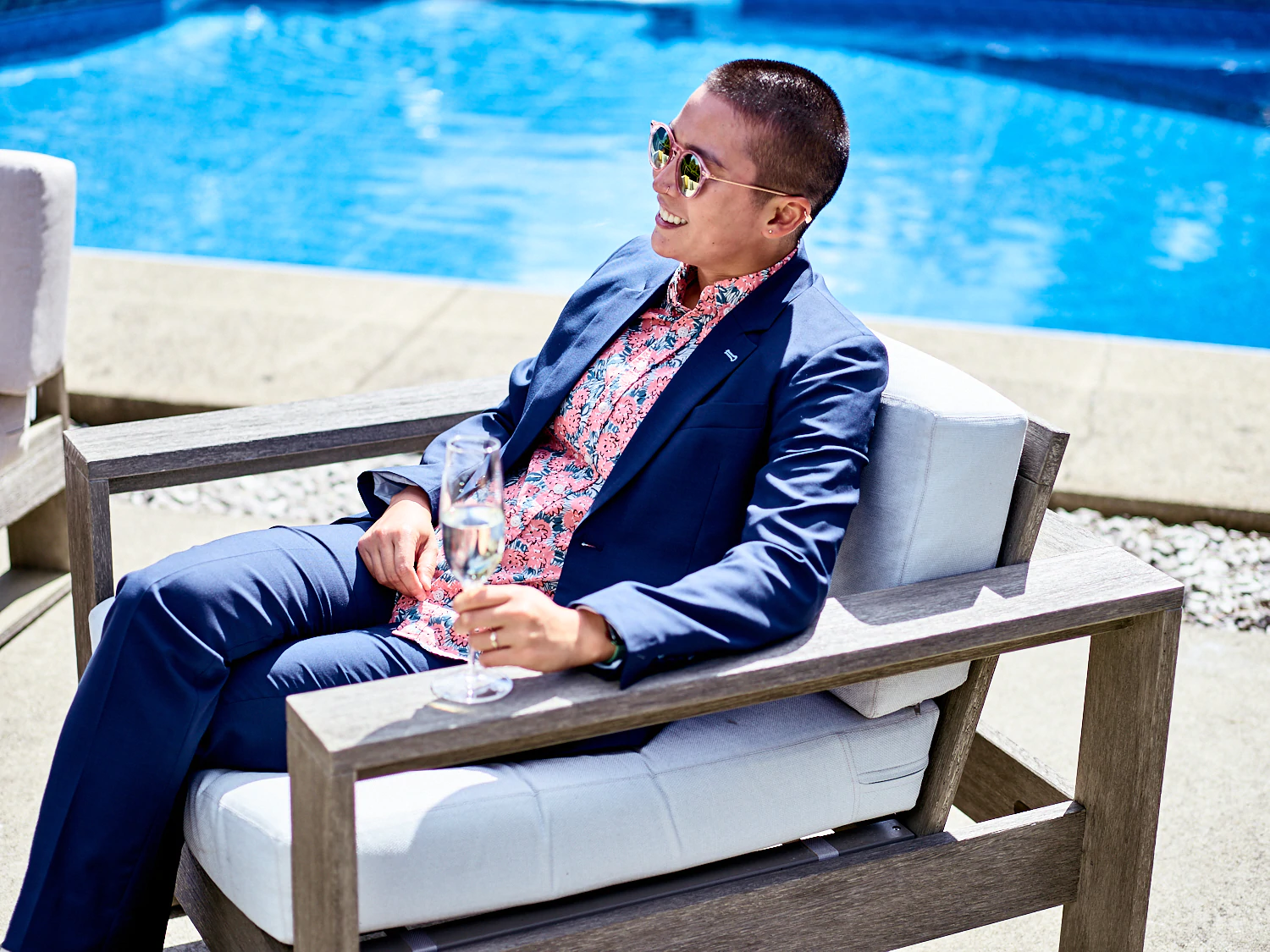 A model in a set of clothing by Kirrin Finch relaxing by the pool with a drink.