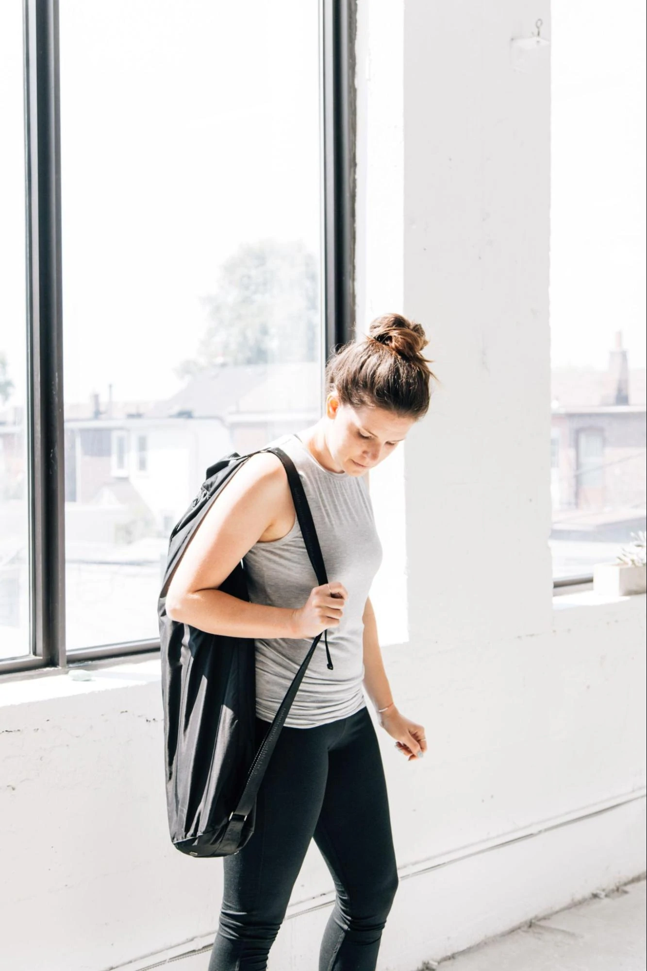 A model in workout clothing carrying a yoga mat bag on one shoulder