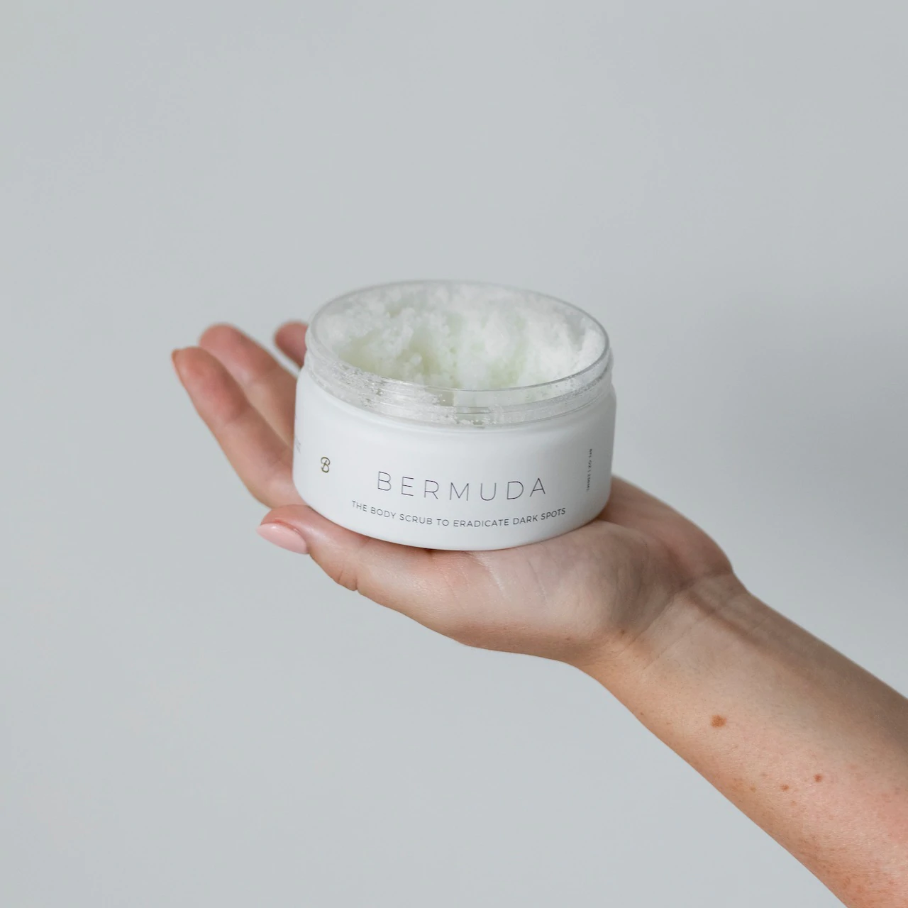 A jar of body scrub by Bushablm held by a hand model.