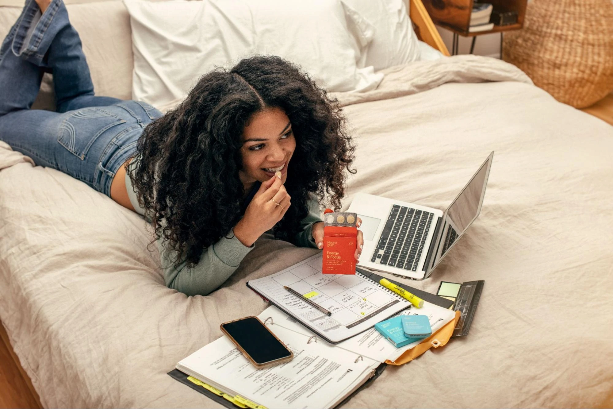 Una modella che studia a letto mentre tiene in mano un pacchetto di gengive Neuro.