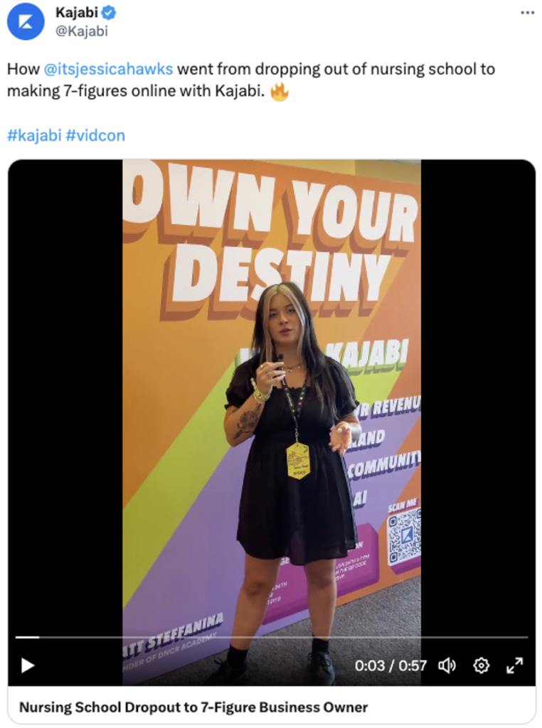 Uma captura de tela de uma postagem X de Kajabi. O texto da postagem diz: “Como @itsjessicahawks deixou de abandonar a escola de enfermagem e passou a ganhar 7 dígitos online com Kajabi. #kajabi #vidcon.” A imagem da postagem é um vídeo de Jessica Hawks, uma mulher usando um vestido preto e botas, parada em frente a um grande cenário colorido onde se lê “Own Your Destiny”.